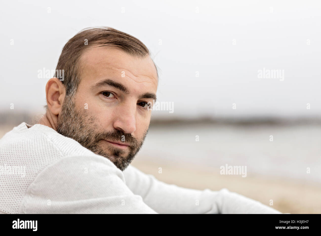 Des hommes (Brunette) avec une barbe dans un chandail blanc face à la mer. Focus sélectif. Banque D'Images