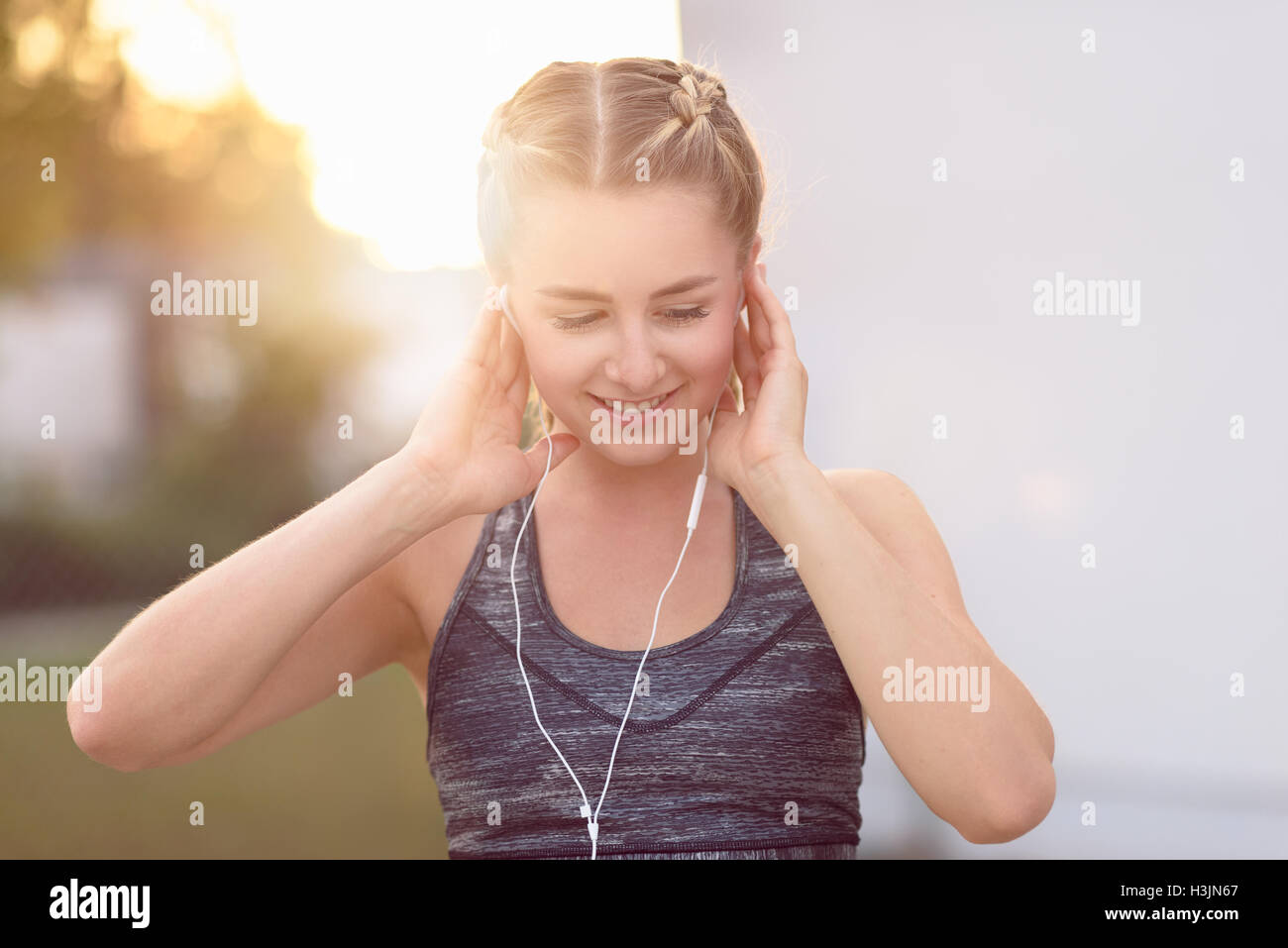 Jolie jeune femme avec un charmant sourire à l'écoute de la musique sur des bouchons d'oreille, un soir d'été à la lueur du soleil couchant Banque D'Images