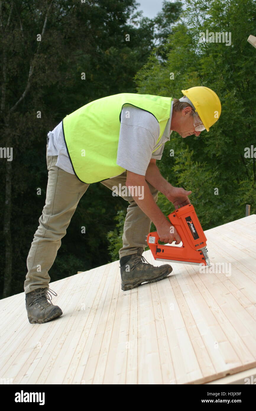 Un travailleur utilise un pistolet à essence pour fixer des plaques pour toiture sur une auto-construction bois maison dans le Kent, UK Banque D'Images