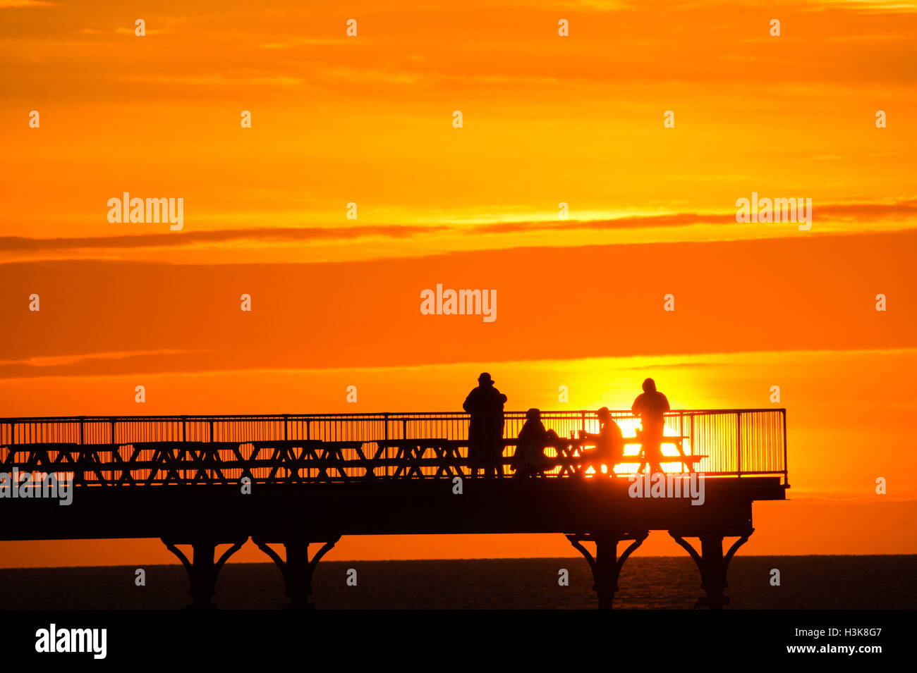 Aberystwyth, Pays de Galles, Royaume-Uni. 9 octobre, 2016. UK Météo : Ciel rouge le soir - à la fin d'une journée de soleil presque sans interruption sur la côte ouest du pays de Galles, un groupe de personnes debout à la fin de l'Aberystwyth station pier, profitez du spectacle d'un coucher de soleil spectaculaire sur la baie de Cardigan Crédit photo : Keith Morris/Alamy Live News Banque D'Images