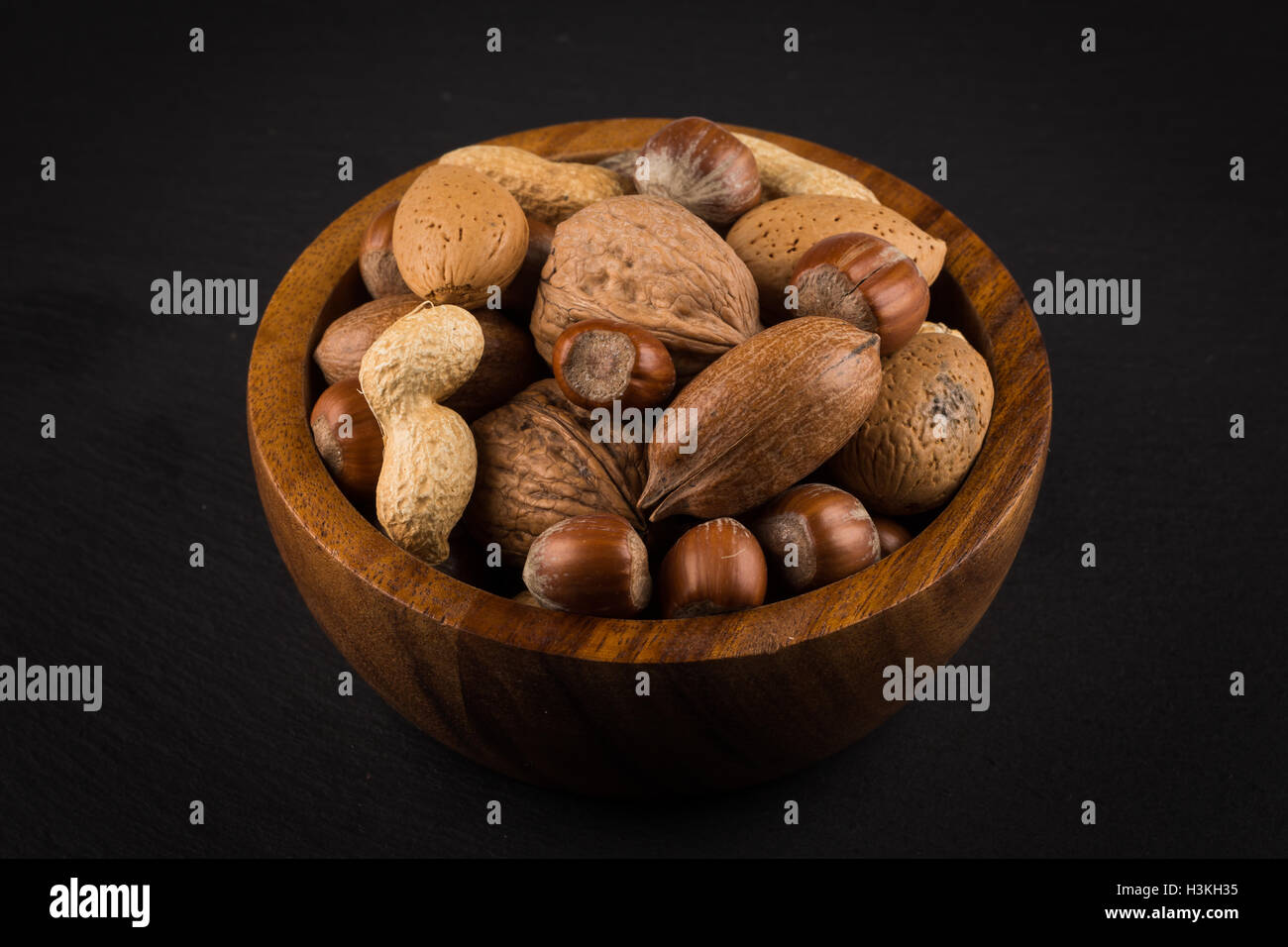 Noix mélangées en coquilles dans un bol une pierre sombre contexte Banque D'Images