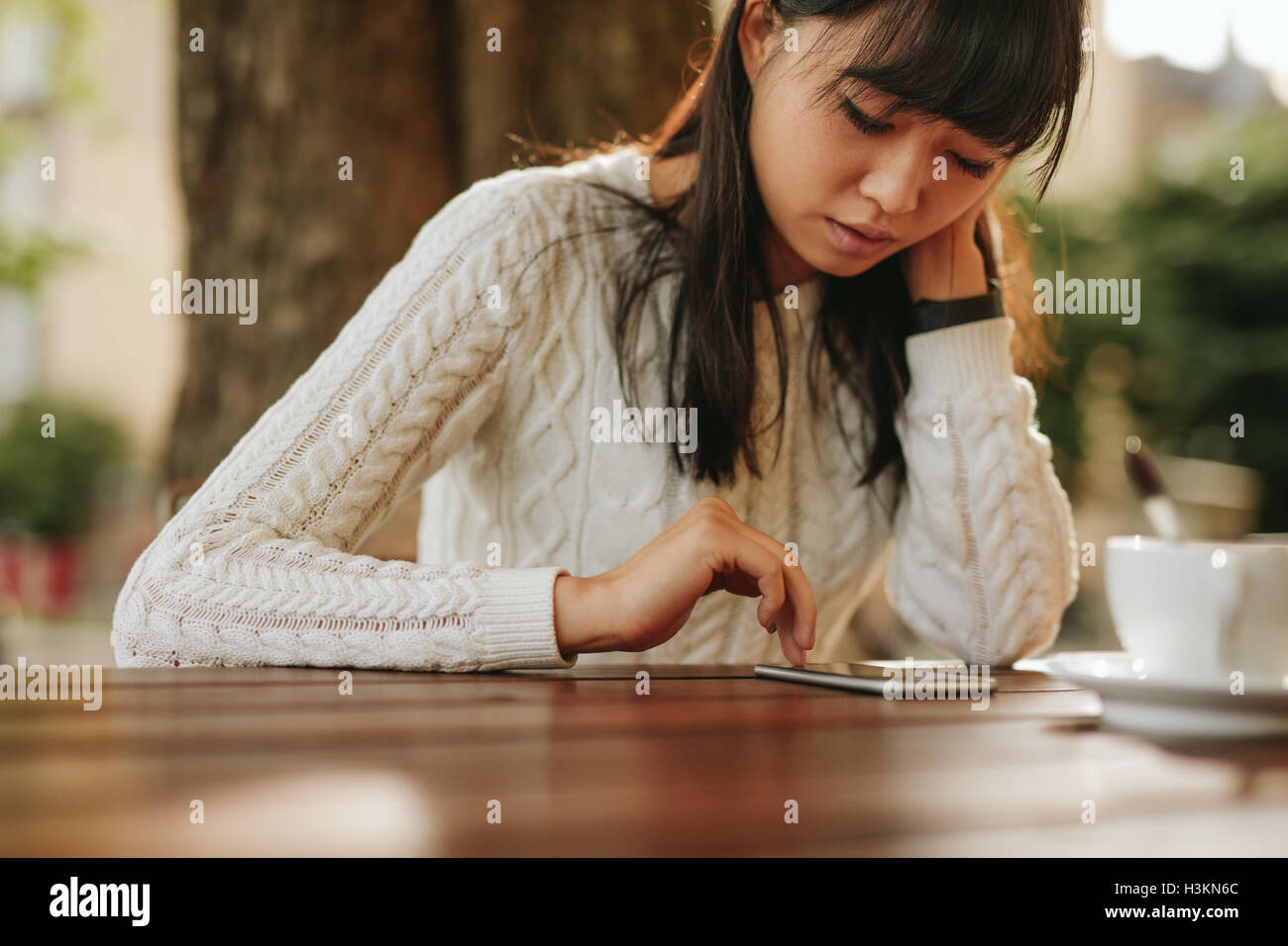 Jeune femme chinoise à la recherche de son portable alors qu'il était assis au café en plein air. Modèle féminin asiatique à l'aide de téléphone mobile à coffeeshop. Banque D'Images