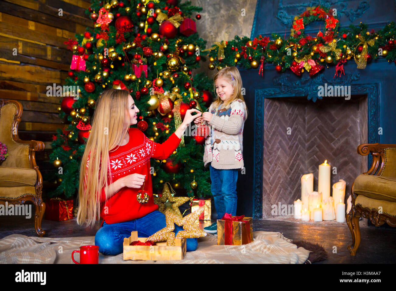 Enfant fille avec mère decorating Christmas Tree à l'intérieur près de cheminée Banque D'Images