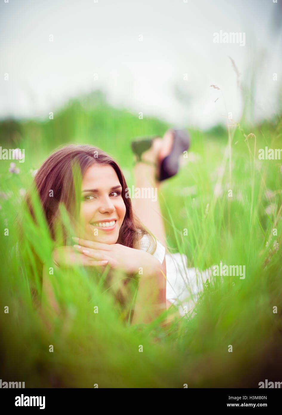 Happy smiling beautiful young woman lying parmi l'herbe et de fleurs Banque D'Images
