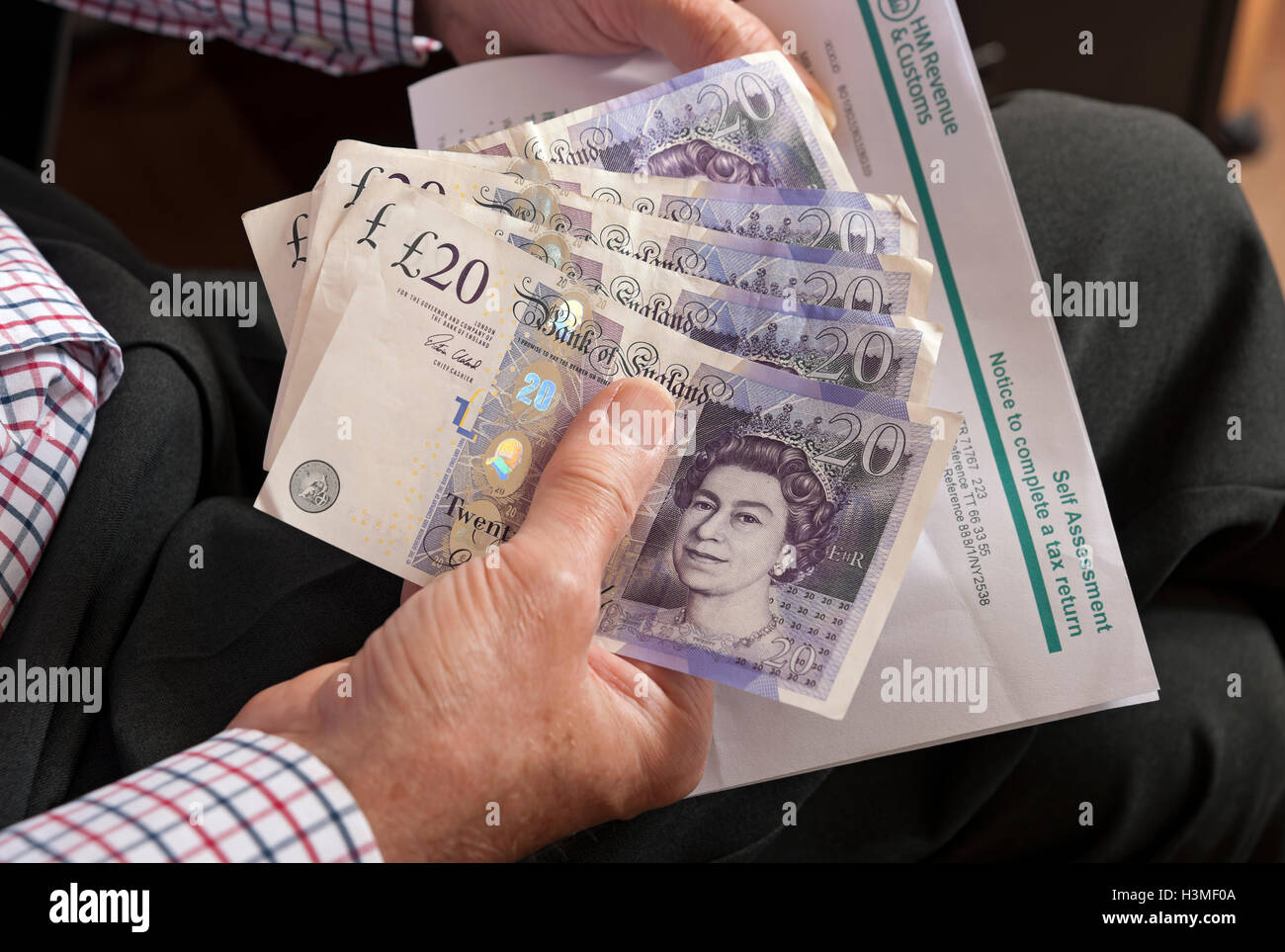 Gros plan de la personne homme détenant vingt billets de banque en argent anglais billets en espèces et déclaration d'auto-évaluation Angleterre Royaume-Uni Grande-Bretagne Banque D'Images