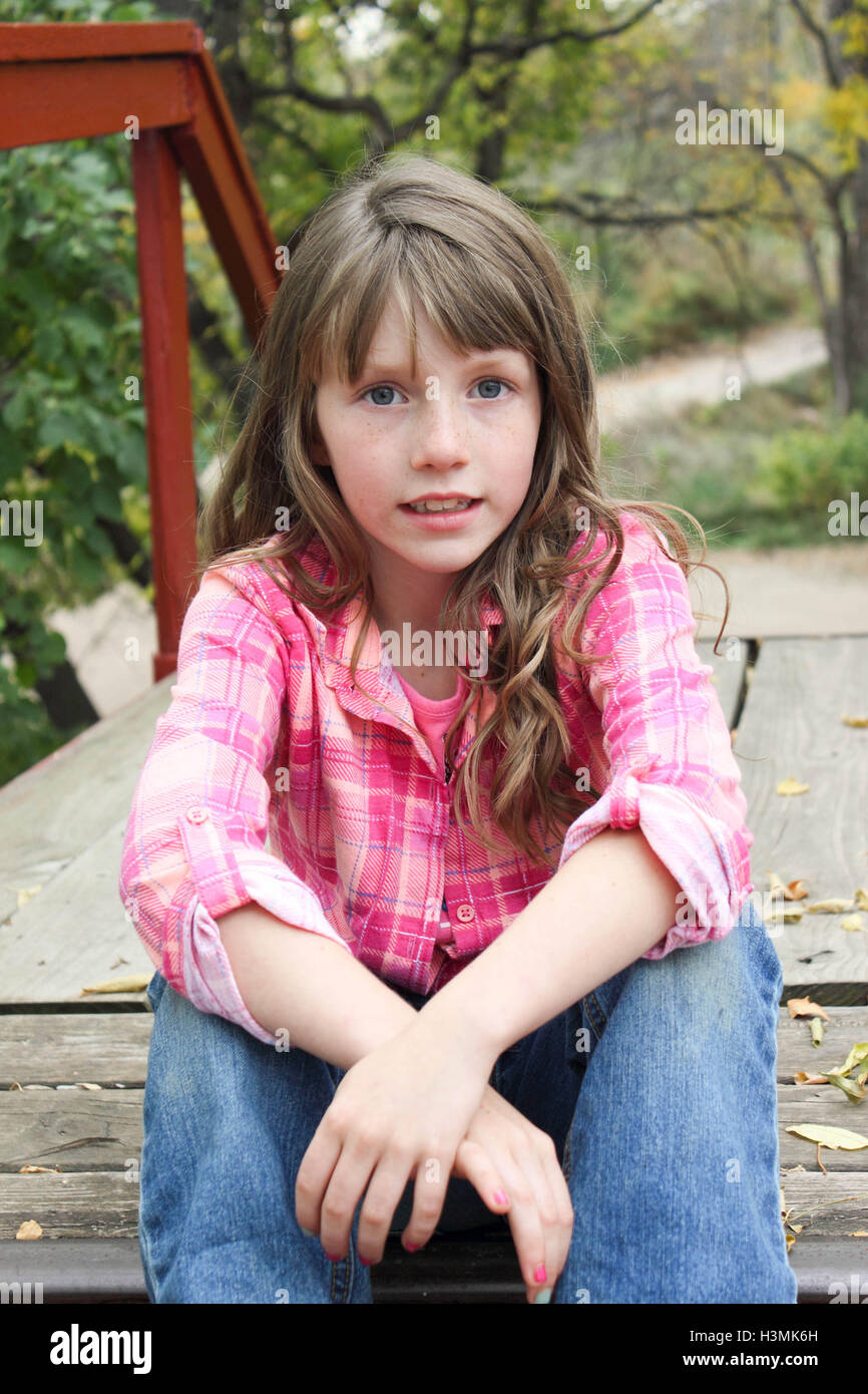 Petite fille assise sur l'escalier en bois coloré en chemise à carreaux roses et posant pour l'appareil photo Banque D'Images