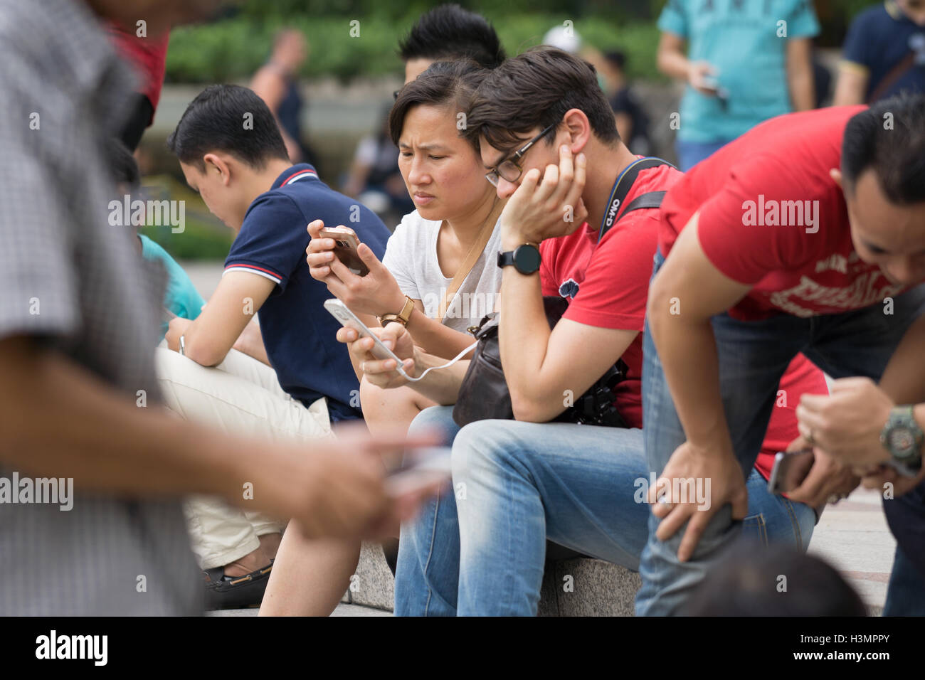 Les gens de l'Asie en utilisant leur téléphone mobile tout en s'asseyant, Malaisie, Kuala Lumpur Banque D'Images