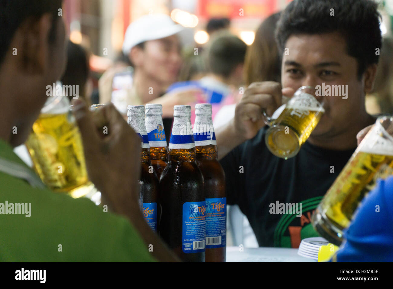 Bouteilles de bière Tiger,sur une table tandis qu'un groupe d'hommes de prendre un verre dans la rue Jalan Alor,Kuala Lumpur Malaisie,. Banque D'Images