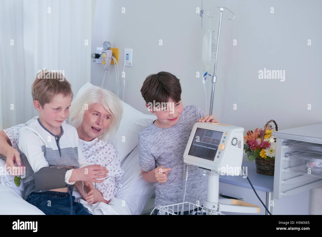 Senior female patient in hospital bed avec petits-fils jouer avec machine à pression artérielle Banque D'Images