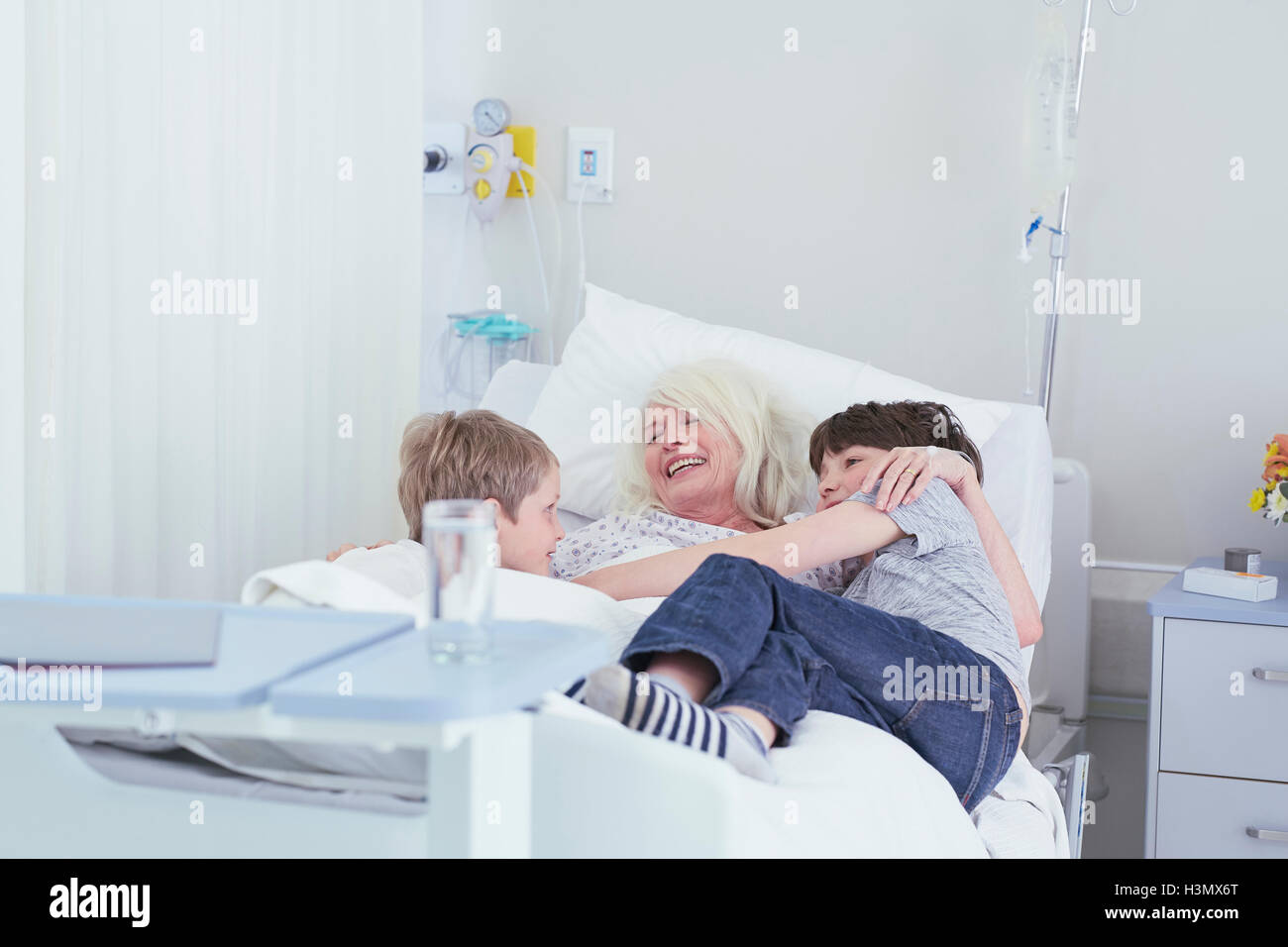 Senior female patient câlins petits-fils sur lit d'hôpital Banque D'Images
