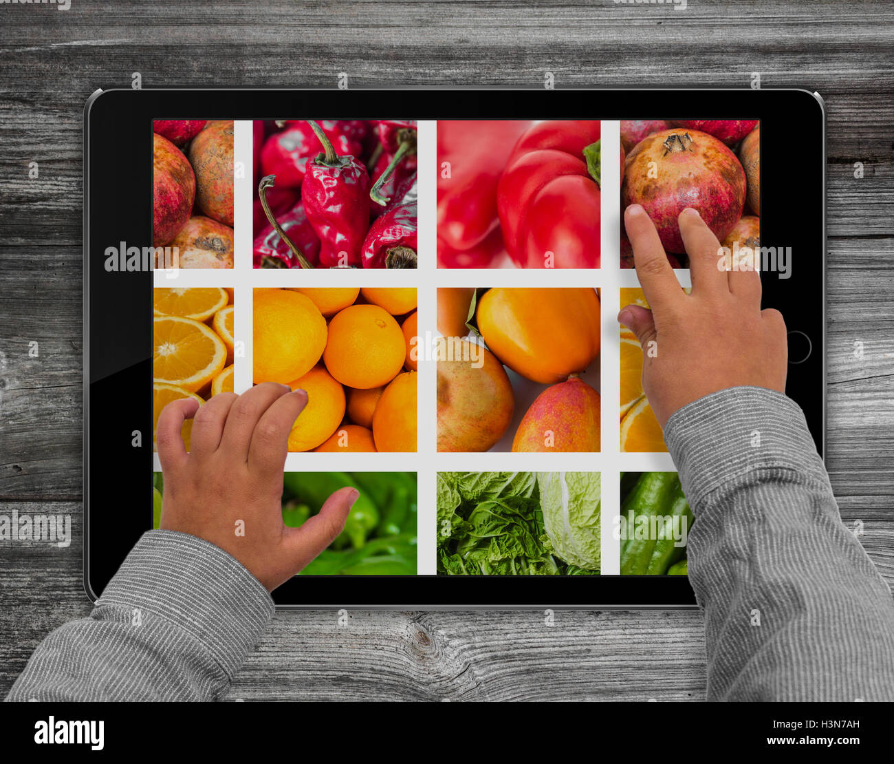 Les mains de l'enfant de toucher l'écran de l'ordinateur tablette avec fruits photo Banque D'Images