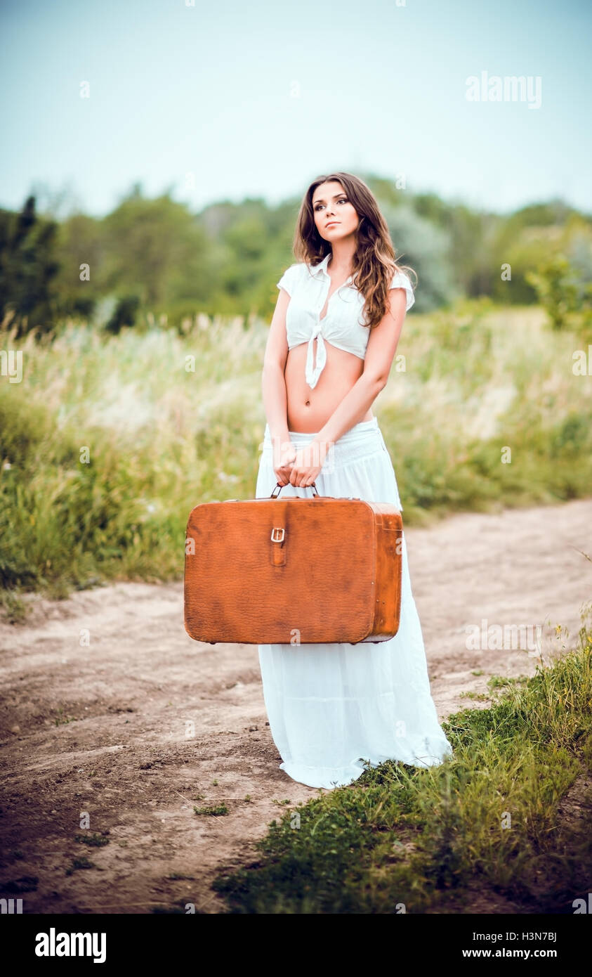 Belle jeune femme avec une valise à la main se tient on rural road Banque D'Images