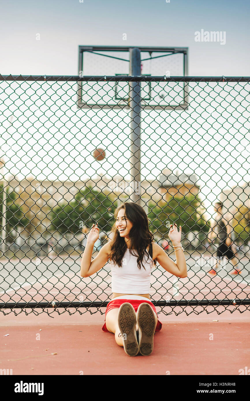 Young woman leaning against fence de basket-ball Banque D'Images