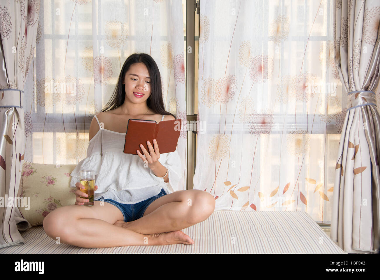 Jeune femme lisant un livre électronique par la fenêtre Banque D'Images