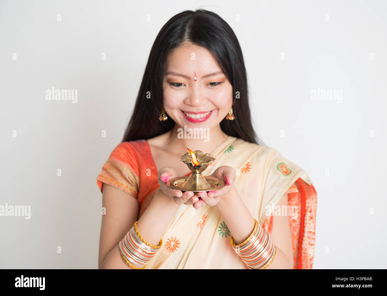 Portrait of young mixed race girl Chinois Indien en sari traditionnel robe, holding diwali lampe à pétrole léger, sur fond uni. Banque D'Images