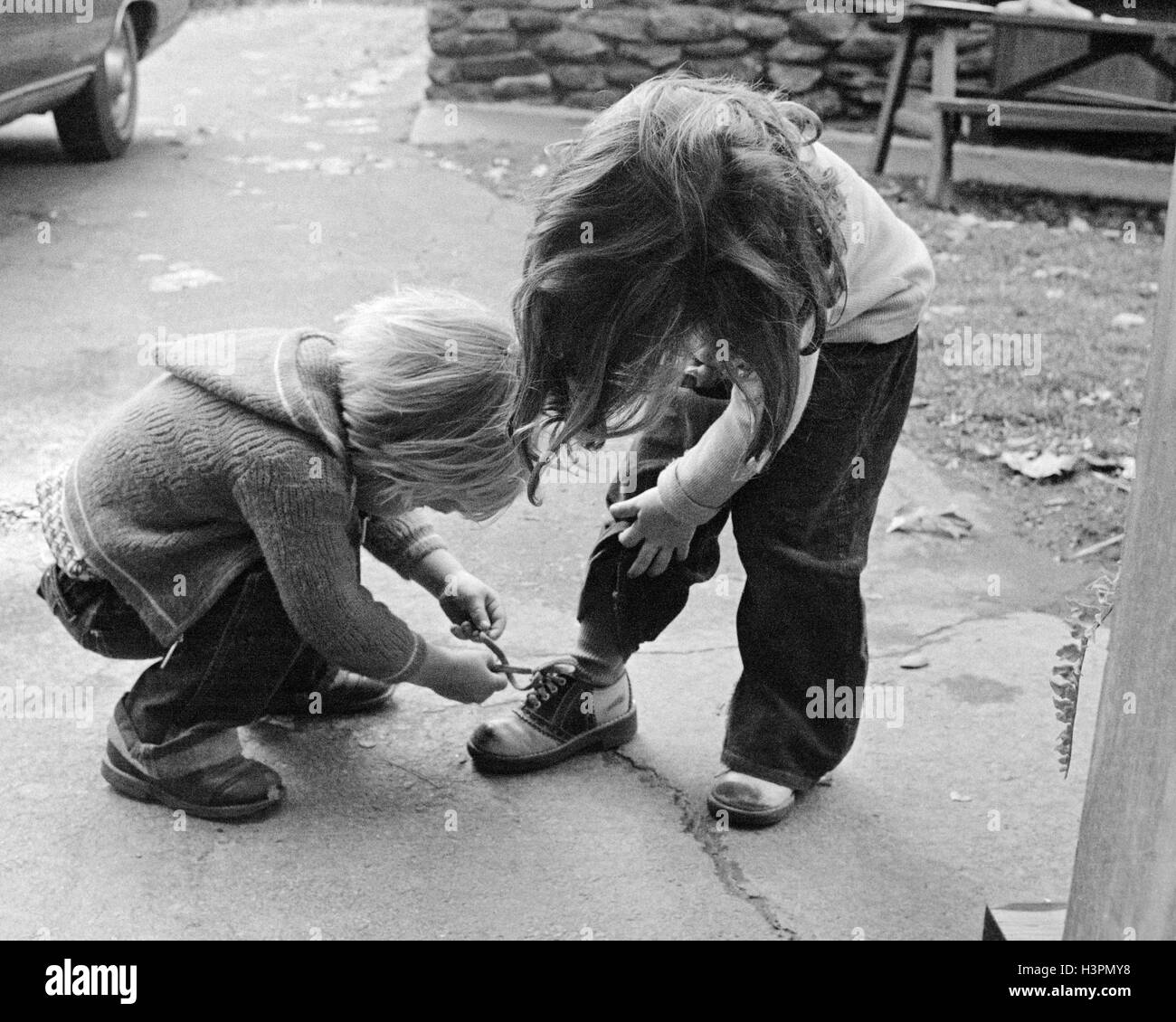 Années 1970 Années 1970 garçon blond se plier plus AIDER GIRL ATTACHER SA CHAUSSURE Banque D'Images