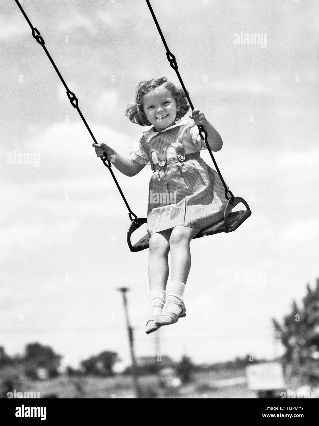 Années 1930 Années 1940 SMILING GIRL ON SWING OUTDOOR LOOKING AT CAMERA Banque D'Images