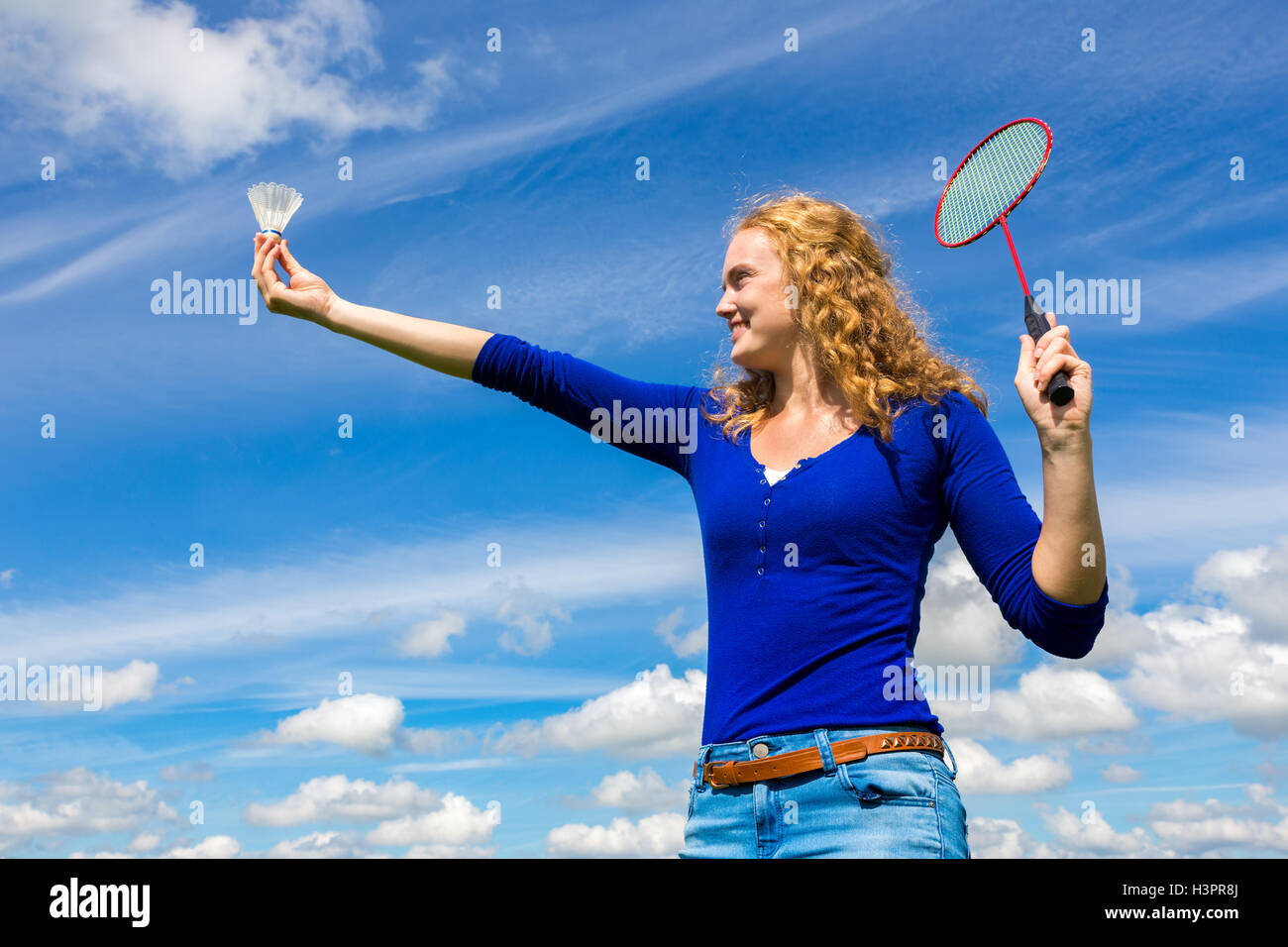 Young caucasian woman holding navette aéroport et badminton racket contre le ciel bleu avec des nuages blancs Banque D'Images