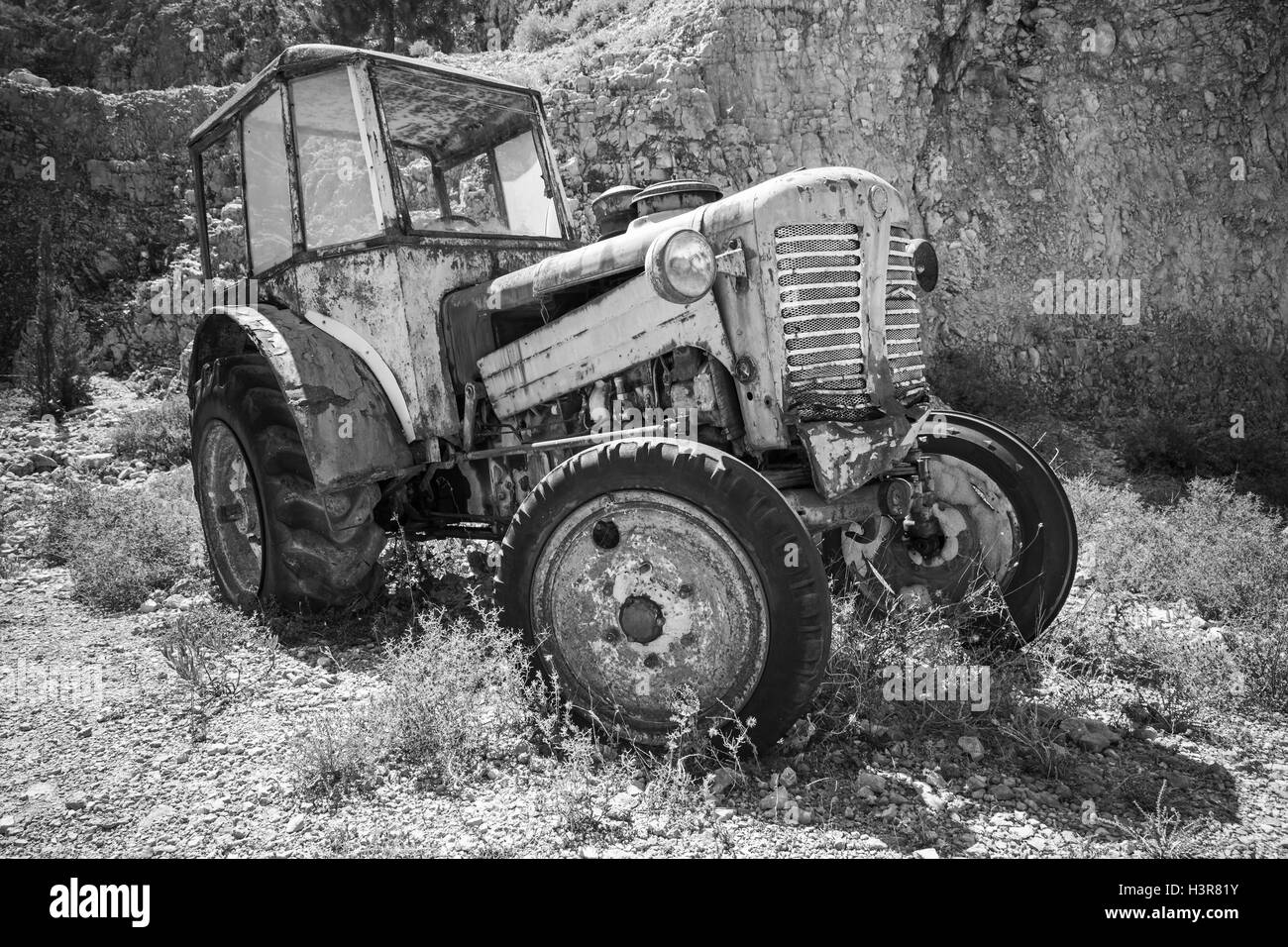 Vieux tracteur rouillé abandonné se dresse sur l'herbe sèche. Photo en noir et blanc Banque D'Images