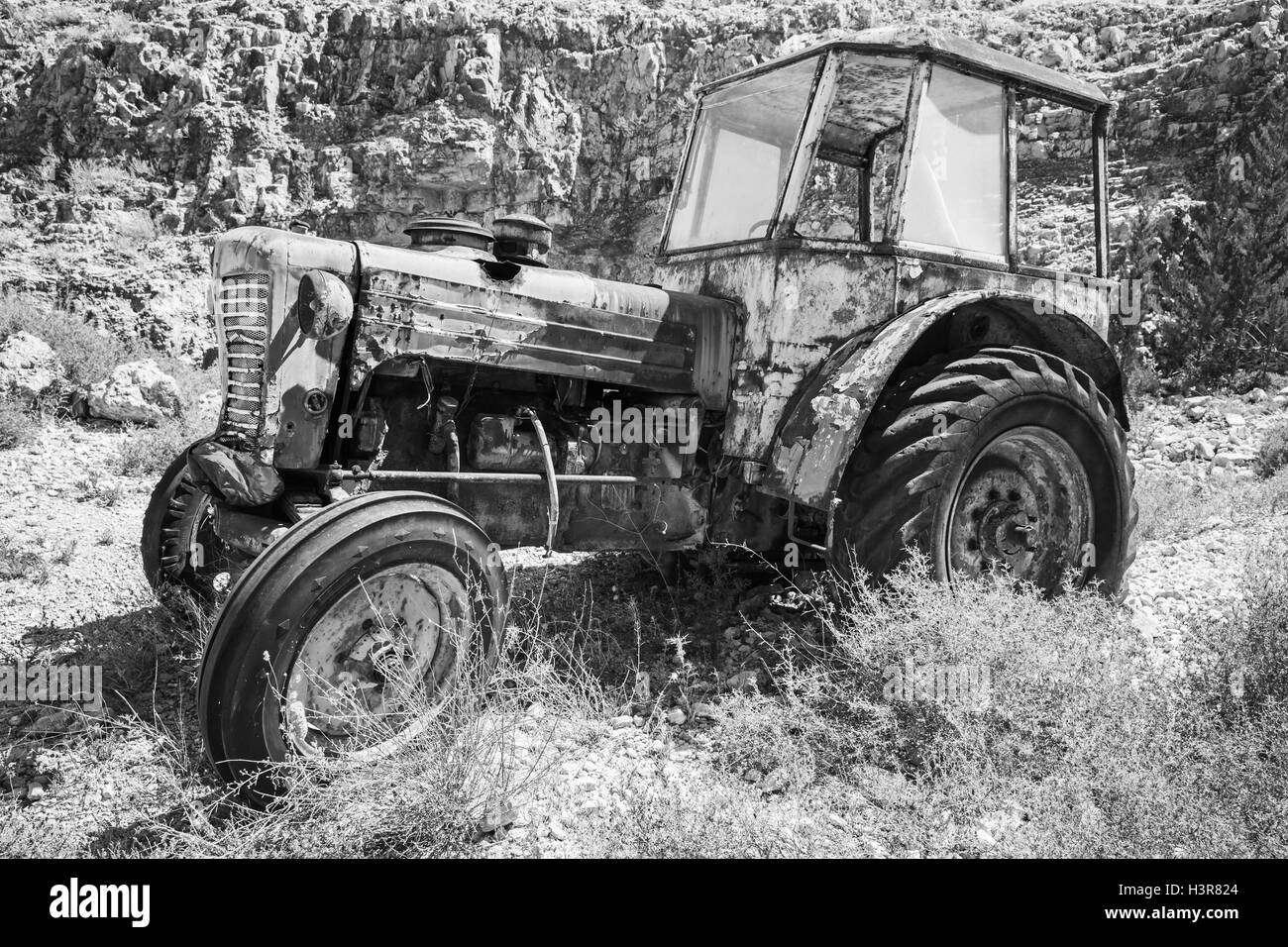 Vieux tracteur rouillé abandonné se dresse sur l'herbe sèche, vue de côté. Photo en noir et blanc Banque D'Images