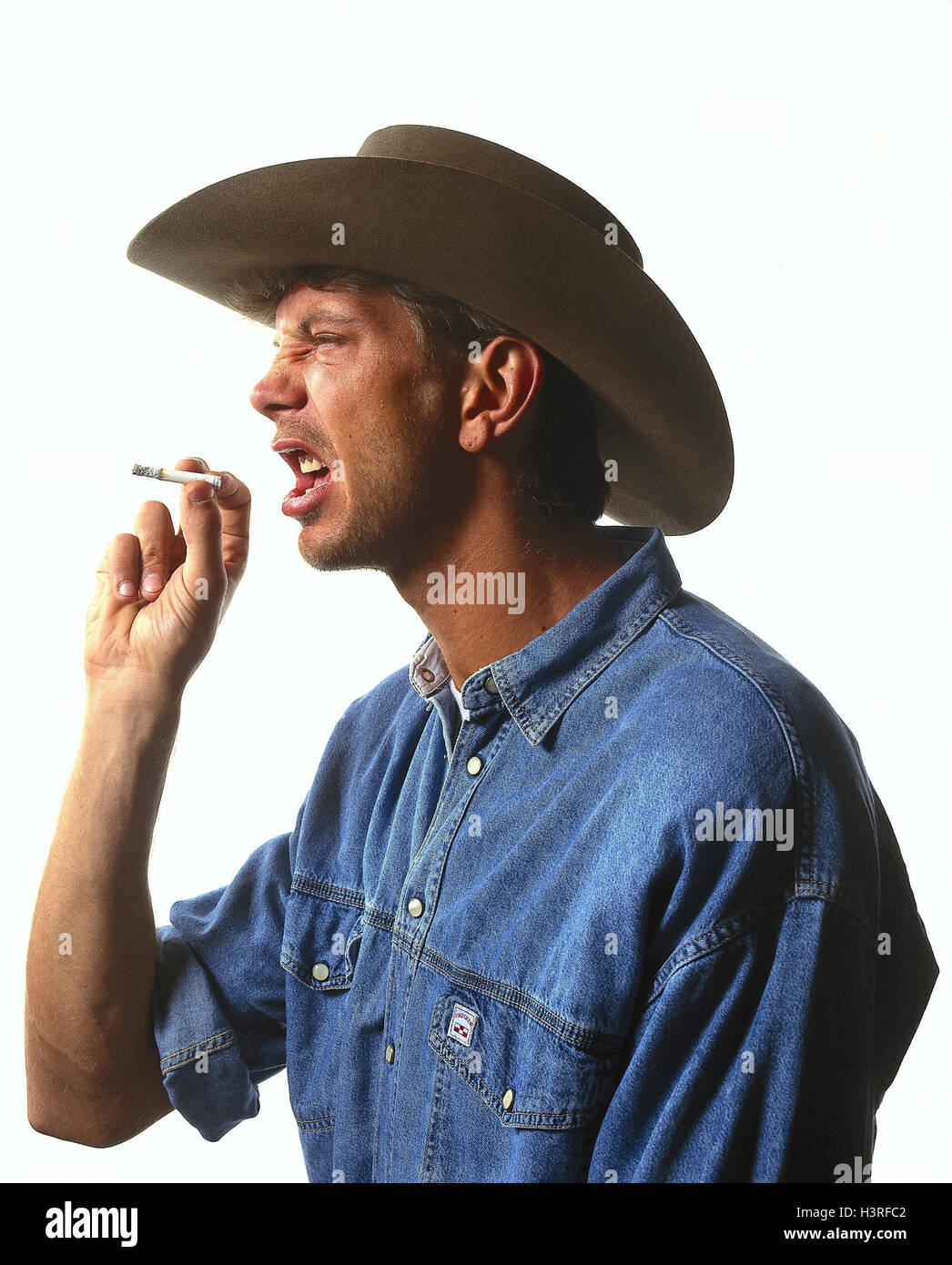 L'homme, stetson, cigarette, jouer du visage, scepticisme, portrait, à l'intérieur, les jeunes, jeans, shirt, férocement hostilely, méfiance, distrustfully, de discorde, irritable, Miss-agace, avec humour, d'ennui, insatisfait, irritable, avec lassitude, de haine, de dégoût, de surabondance, dis Banque D'Images