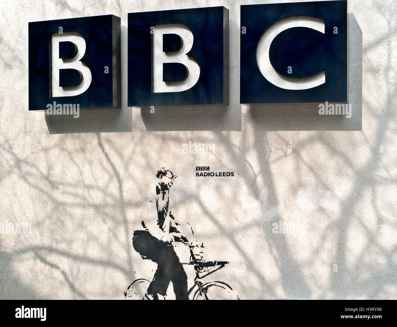 BBC signe à Leeds avec graffiti studio de l'homme sur la location et les ombres de branches d'arbre sur le mur Banque D'Images