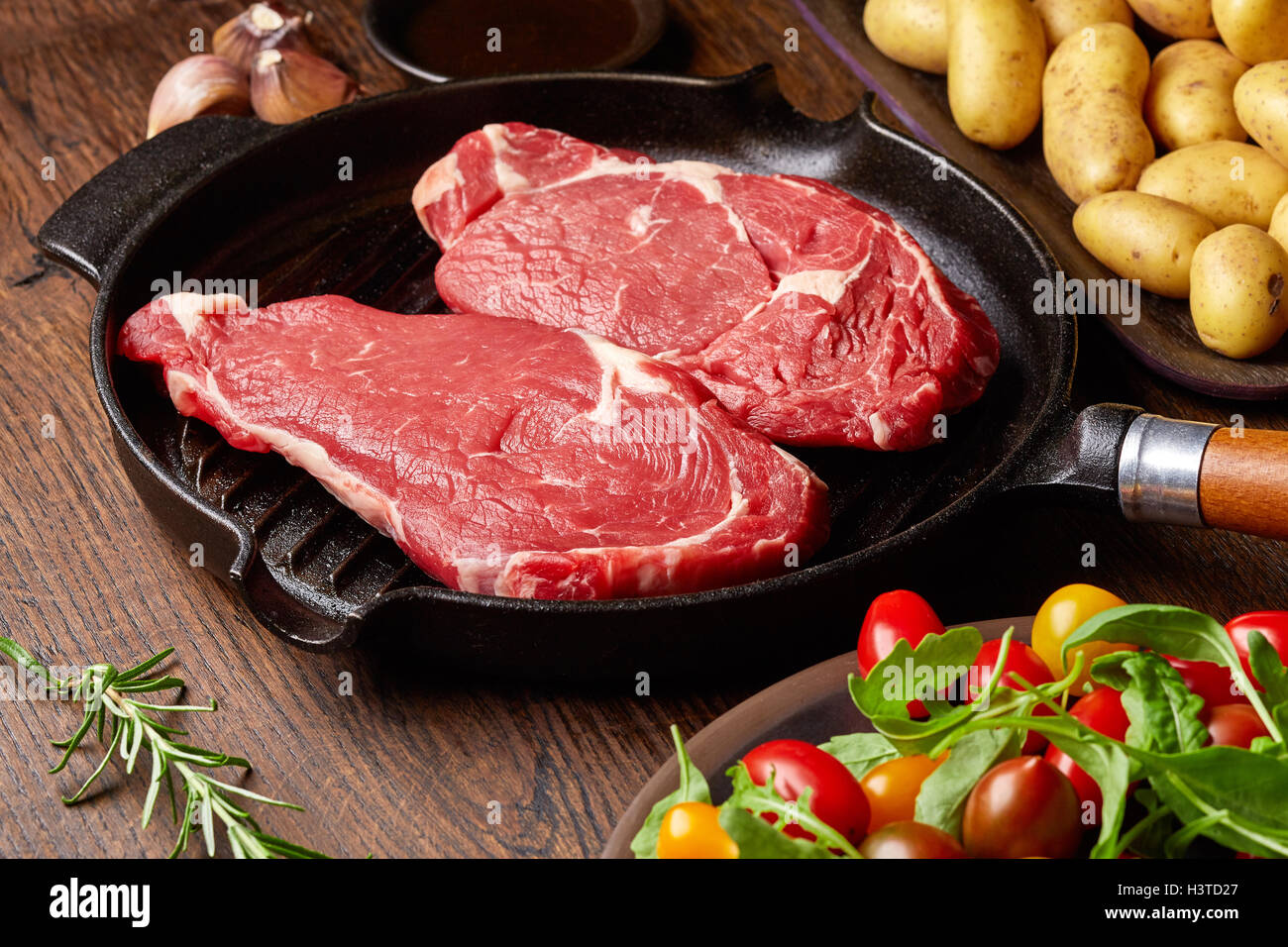 Steak de boeuf cru sur gril, pommes de terre, les épices et les tomates de table en bois Banque D'Images