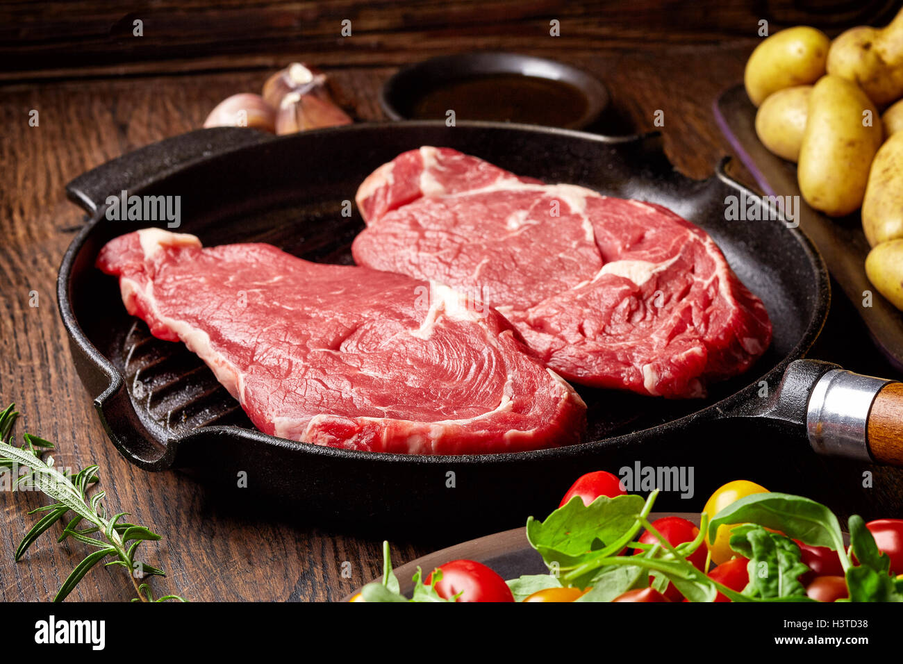 Steak de boeuf cru sur gril, pommes de terre, les épices et les tomates de table en bois Banque D'Images