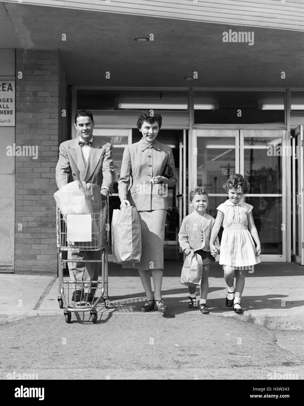 1950 FAMILLE DE QUATRE EN SORTANT D'ÉPICERIE PÈRE SHOPPING SACS DE TRANSPORT, MÈRE ET FILS Banque D'Images