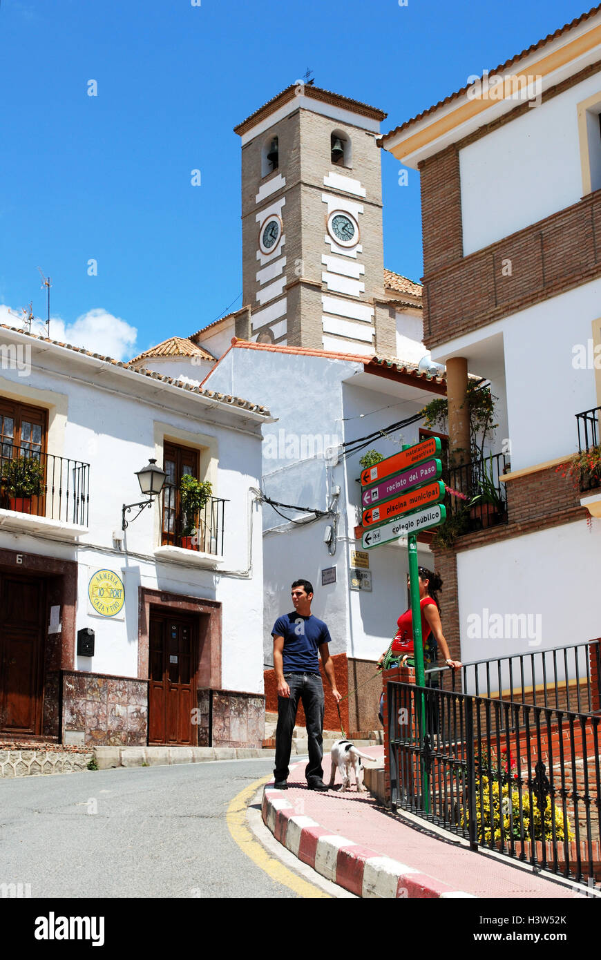 Couple avec un chien debout sur un coin de rue avec l'église à l'arrière, Rio Gordo, Province de Malaga, Andalousie, Espagne, Europe. Banque D'Images