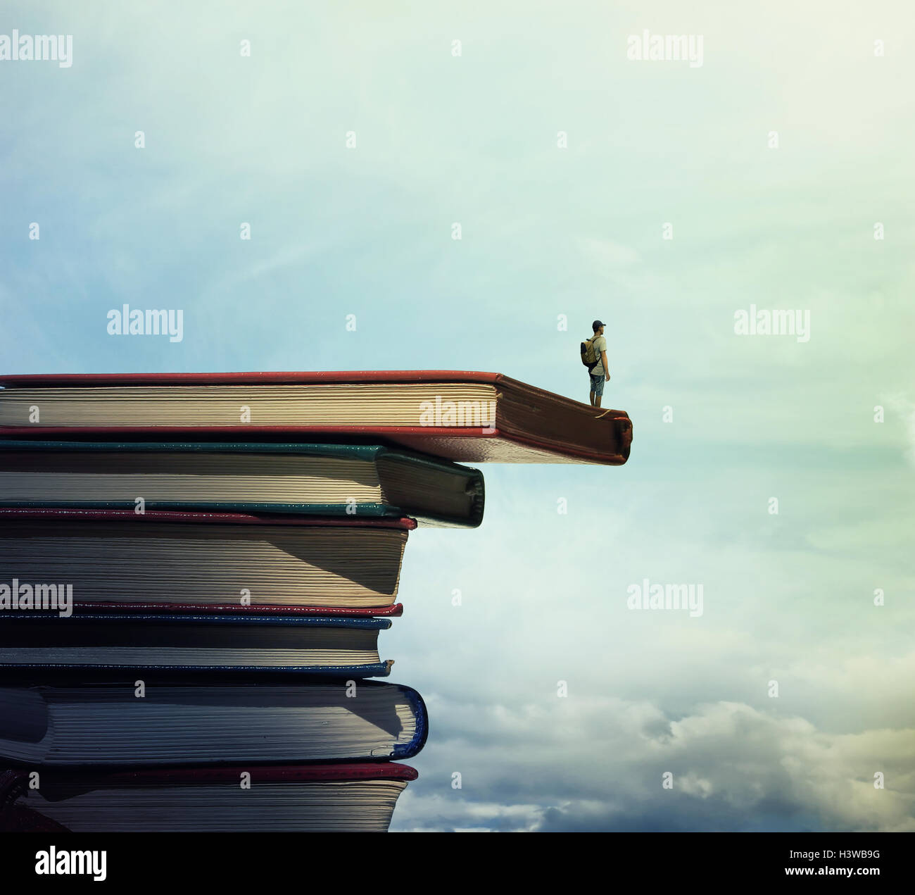 Jeune garçon avec un sac sur son dos se tenir sur une pile de livres à la mesure à l'horizon. À la recherche d'apprendre concept. Banque D'Images