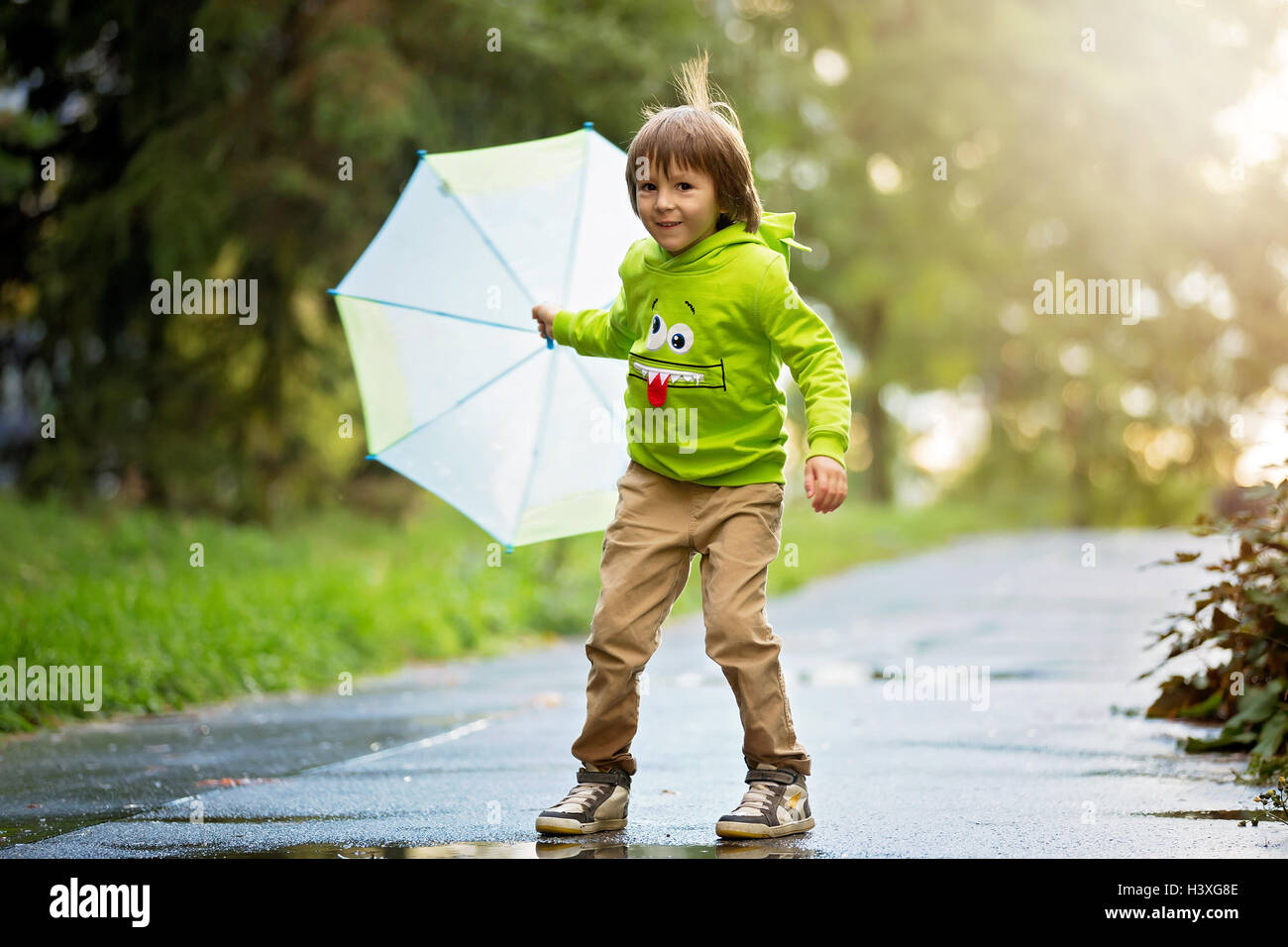 Adorable petit garçon avec parapluie dans un parc un jour de pluie, jouant et sautant, smiling, temps d'automne Banque D'Images