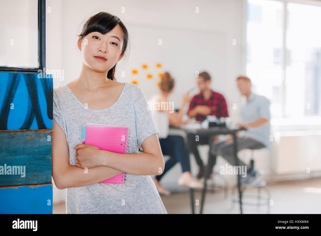 Portrait of young asian business woman standing in office avec les collègues de réunion en arrière-plan. Femme entrepreneur wit permanent Banque D'Images