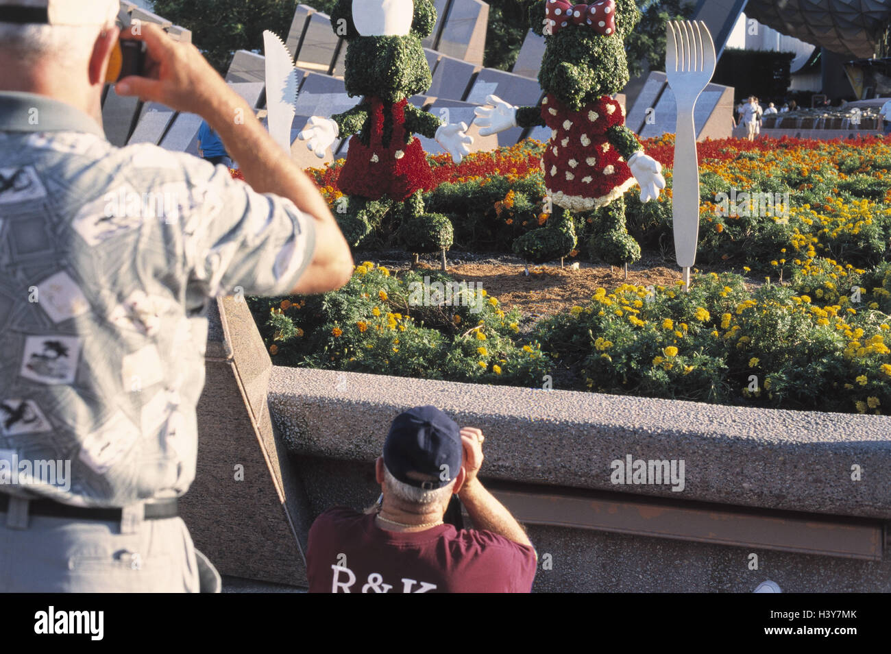 Les USA, Floride, Orlando, Disney-World, parc, les chiffres, les touristes, de prendre une photo, vue arrière du Nord, parc d'amusement, juste, les hommes, les caméras, parc, parterre de fleurs, plante verte, d'une haie, chiffres, chiffres du Disney, fun, du tourisme, de l'endroit d'intérêt Banque D'Images