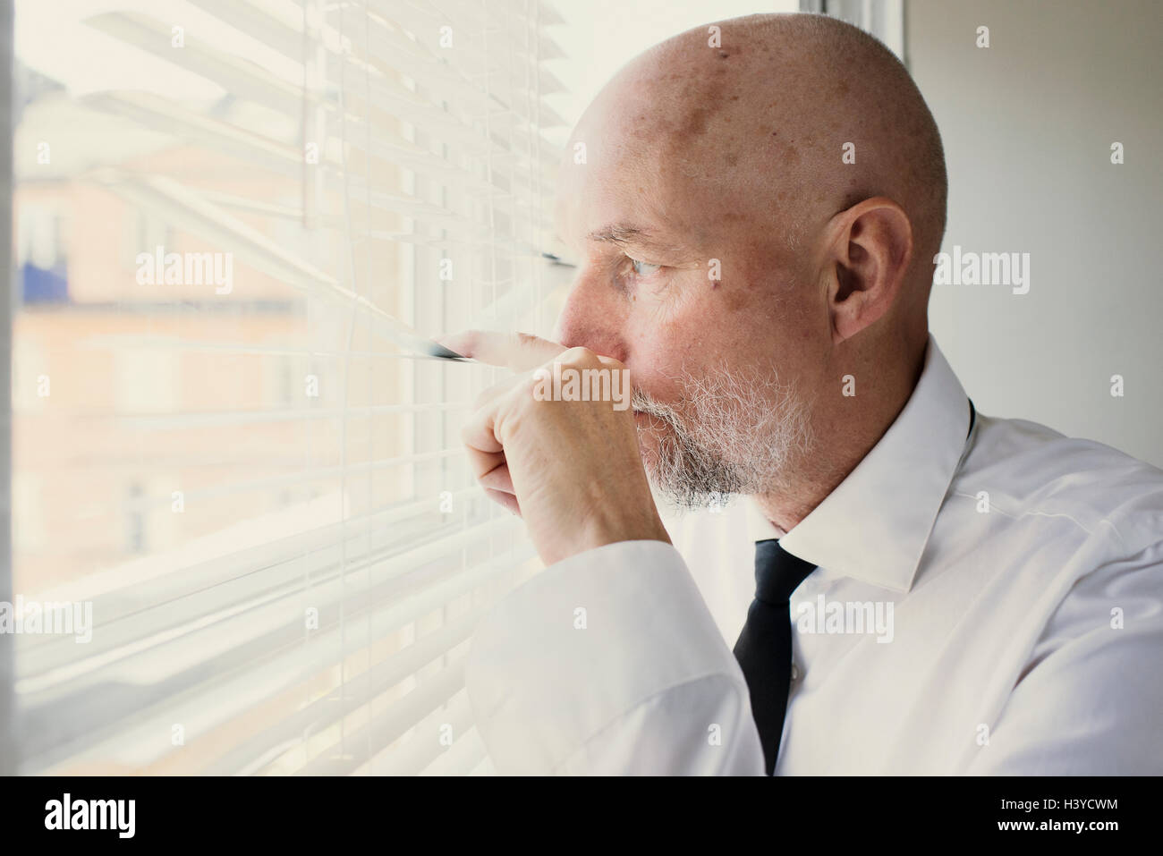 Old man looking out of window through blinds. Concept de l'observation et la surveillance de voisinage. Sentiment d'insécurité dans votre maison. Banque D'Images