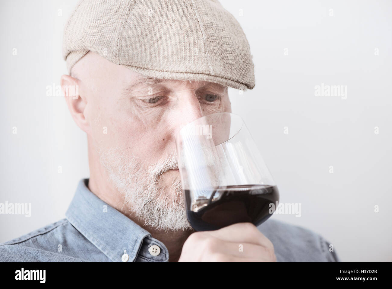 Vieil homme à cap holding wineglass. L'odeur du vin rouge avec sérieux. Banque D'Images
