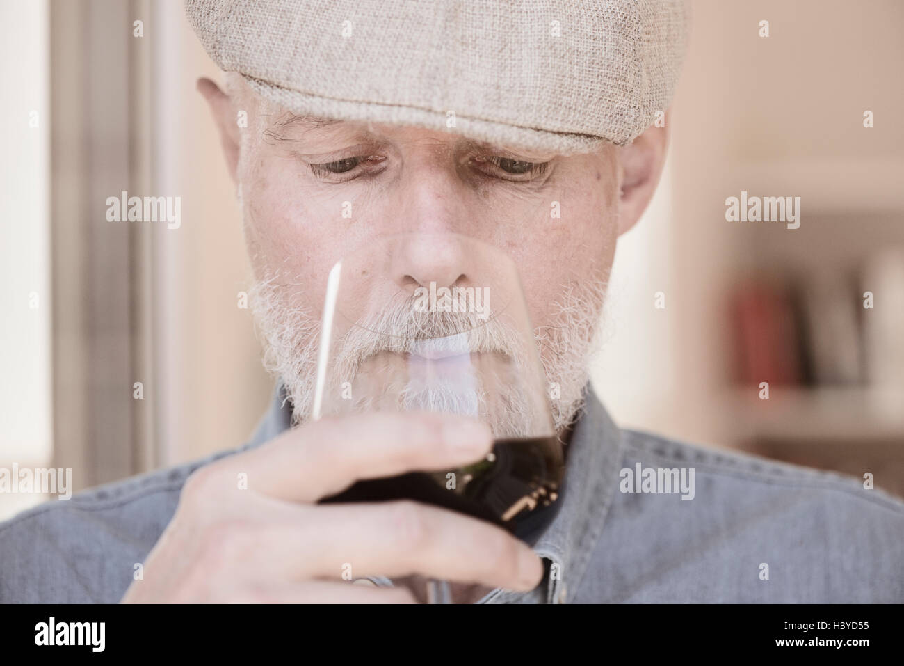Vieil homme à cap holding wineglass. L'odeur du vin rouge avec sérieux. Banque D'Images