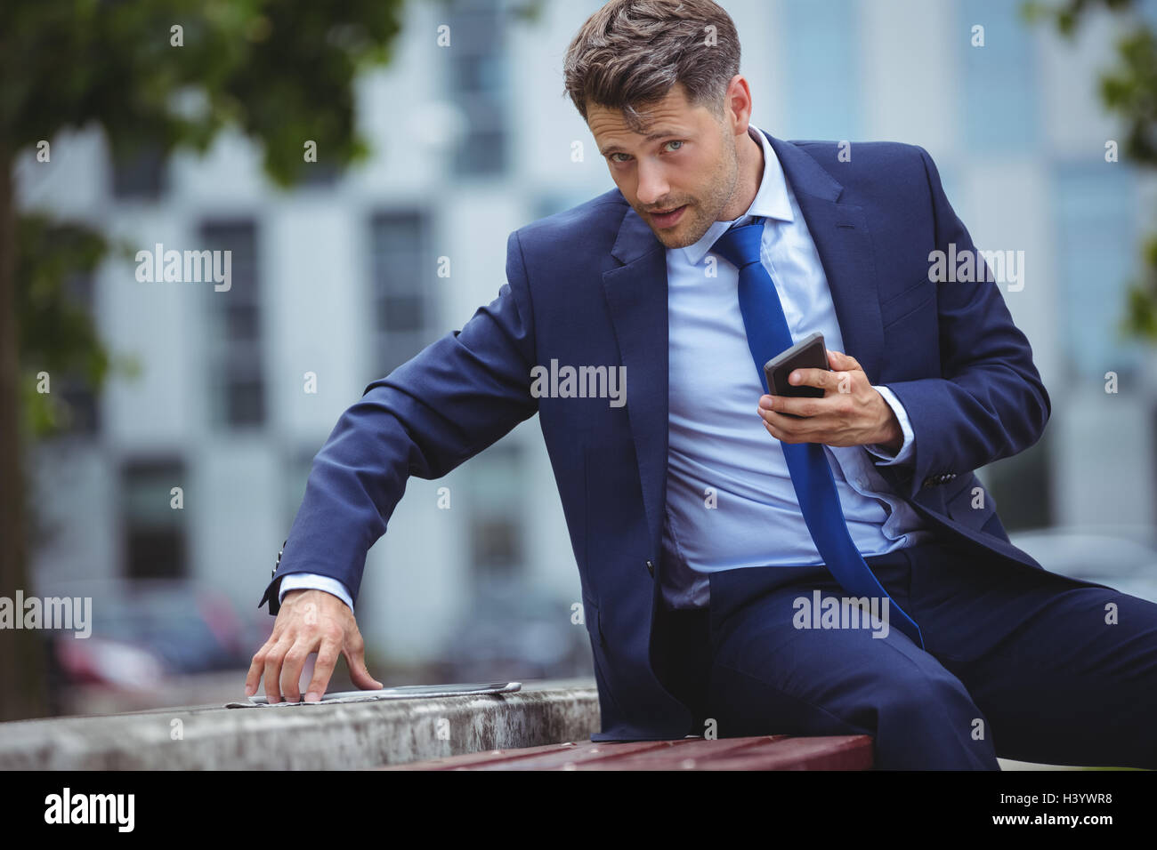 Handsome businessman holding mobile phone while using digital tablet Banque D'Images
