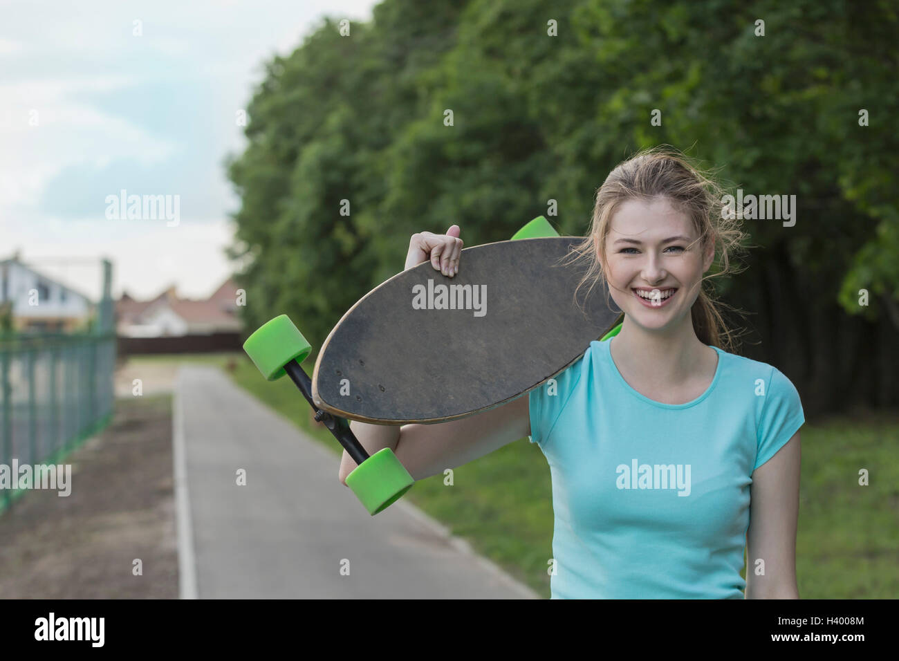 Portrait of cheerful woman holding skateboard debout sur sentier au parc Banque D'Images