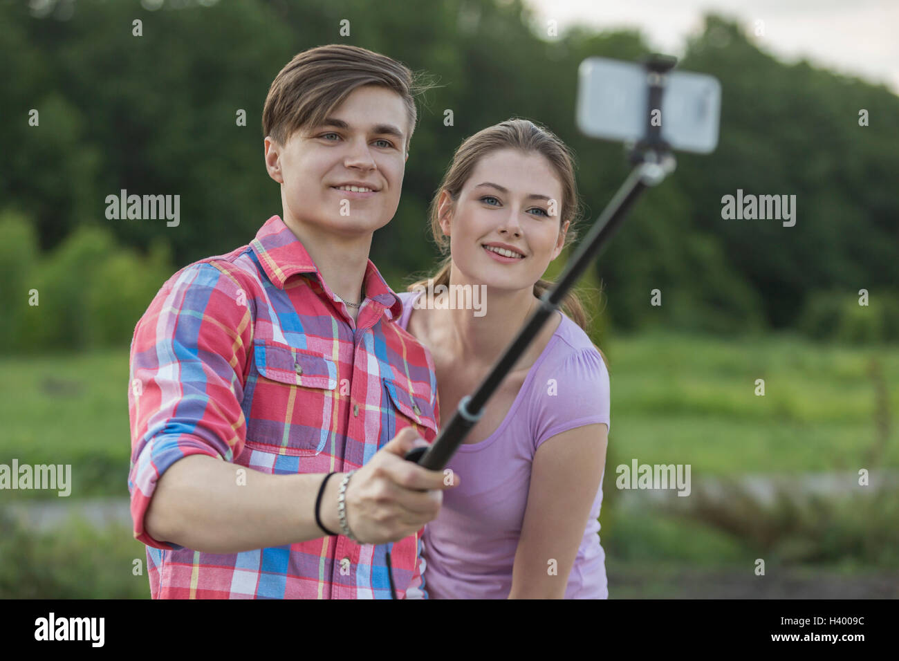 Smiling young couple par selfies monopod au parc contre des arbres Banque D'Images