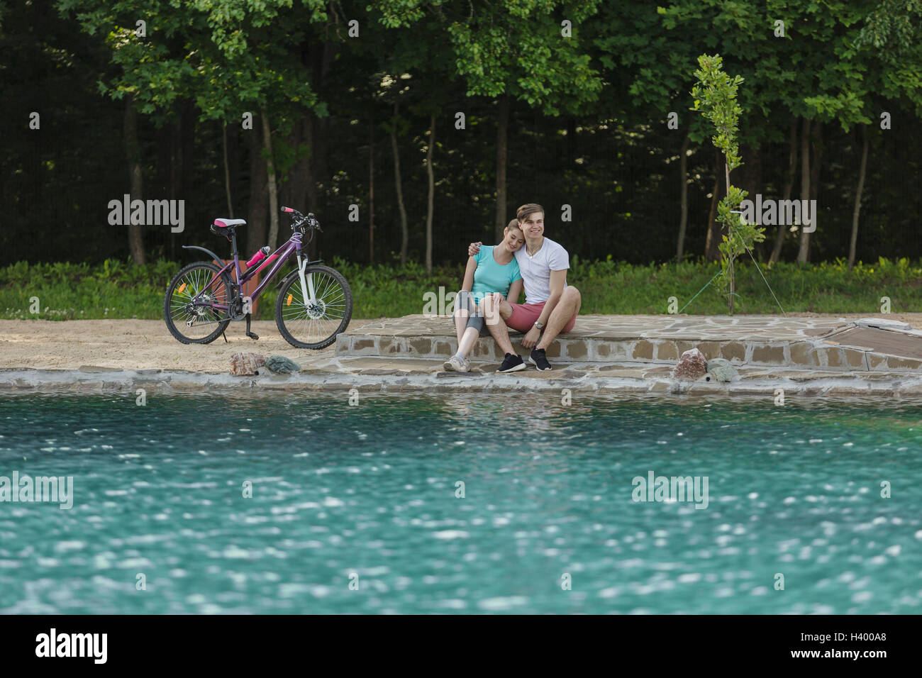 Smiling couple sitting by lake in park Banque D'Images