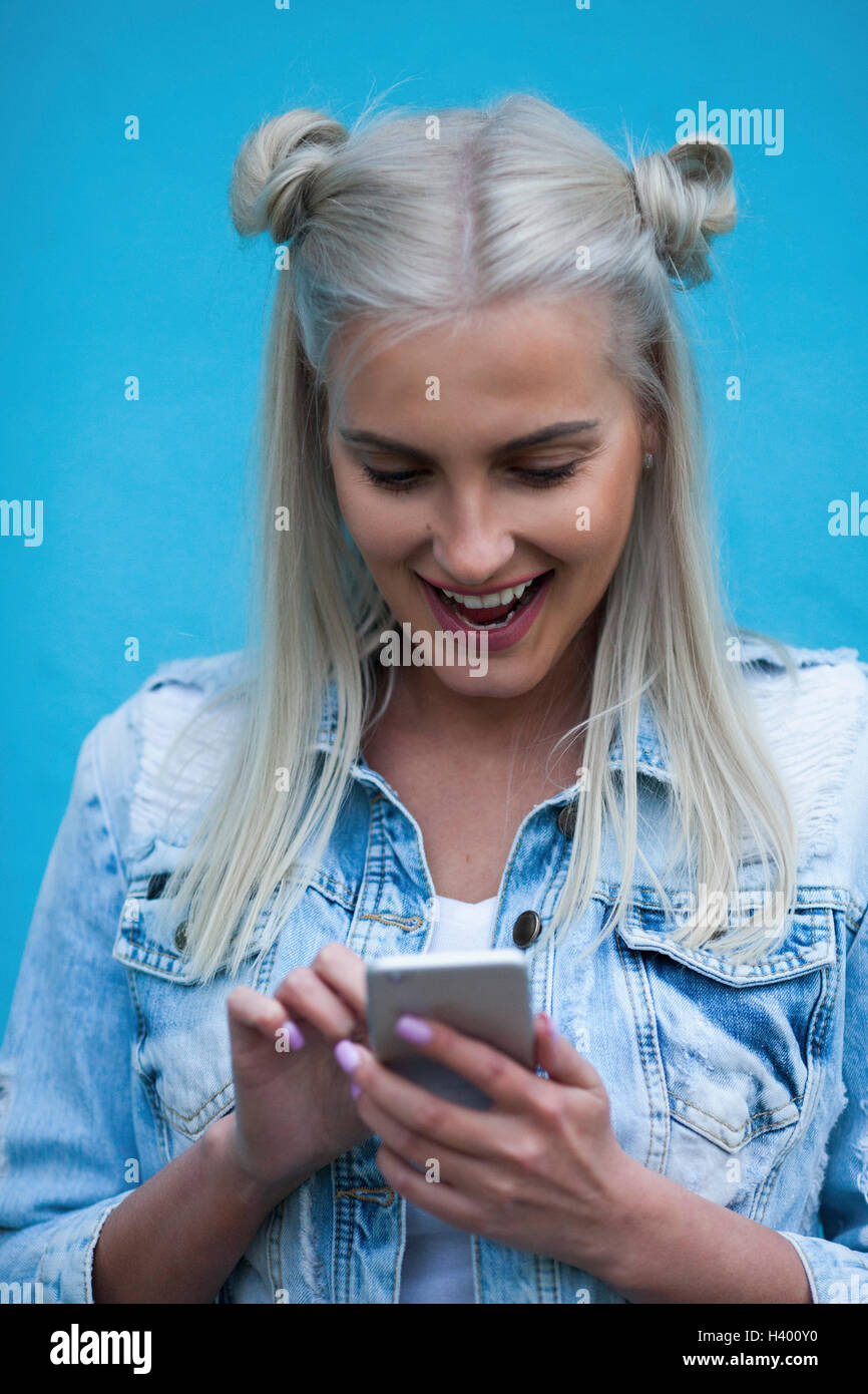 Happy woman using mobile phone contre mur bleu Banque D'Images