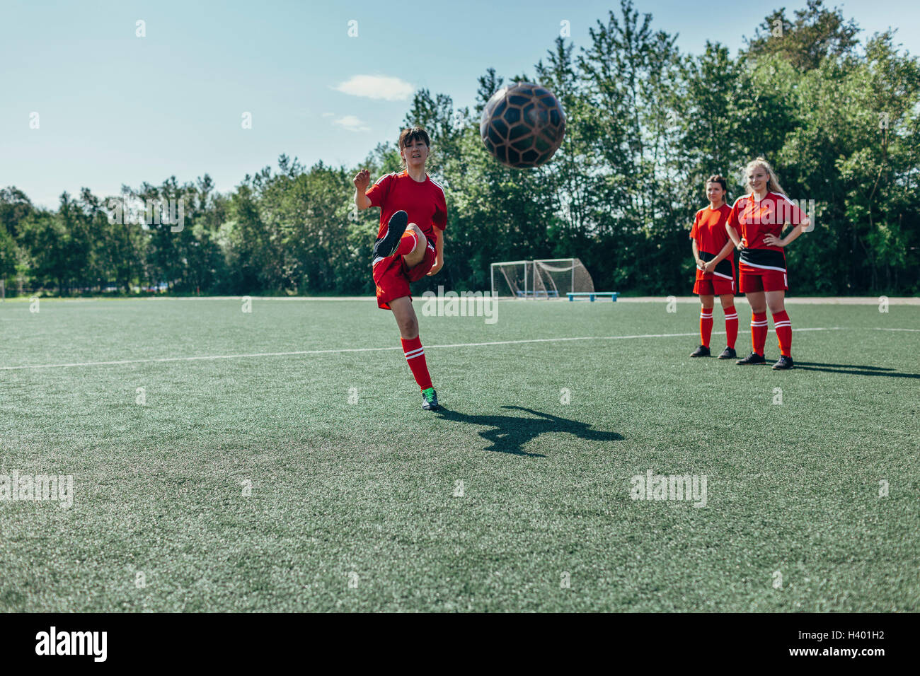 Soccer player kicking ball tandis que ses amis se trouvent à proximité sur terrain Banque D'Images