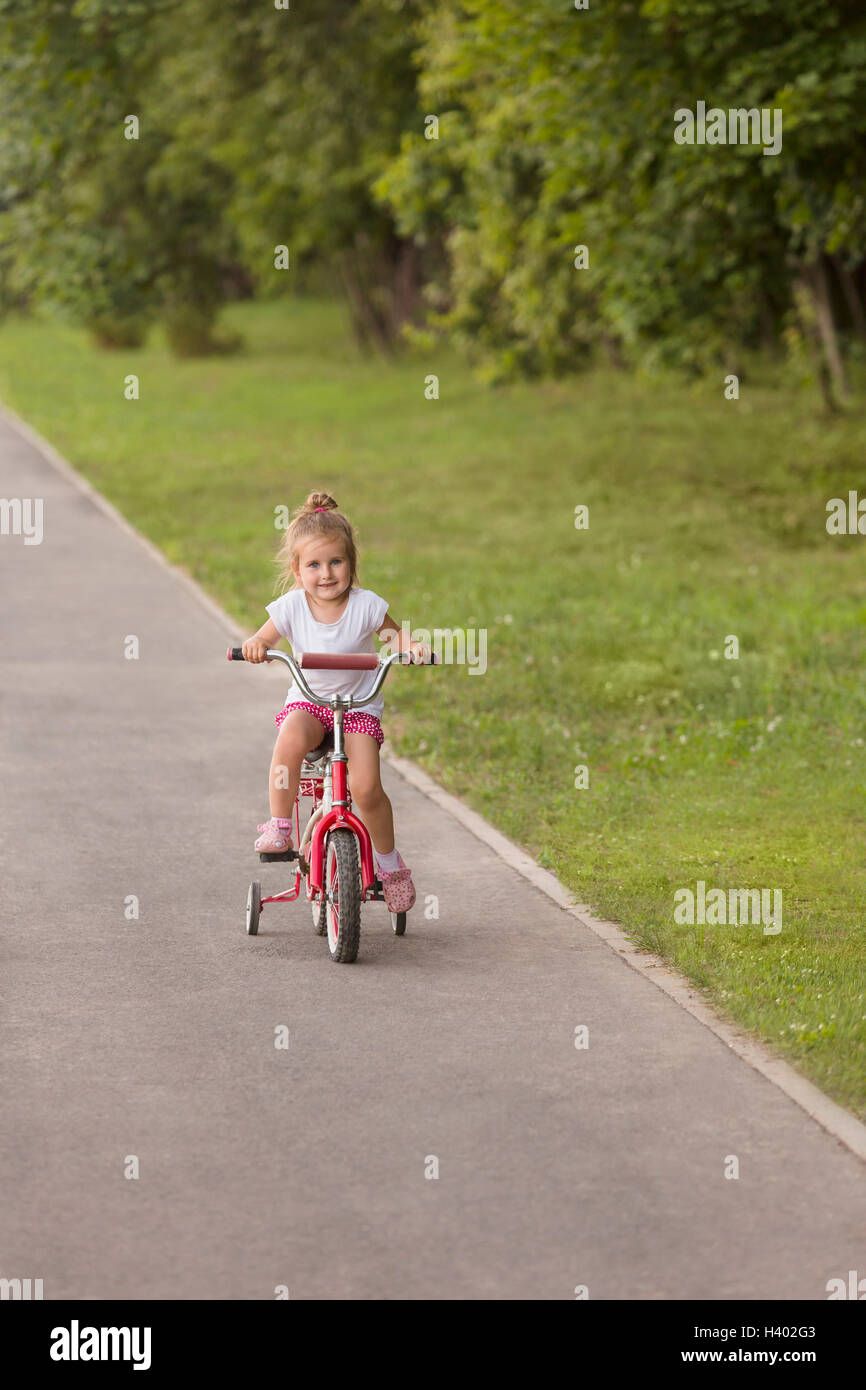 Smiling cute girl vélo sur route par grassy field at park Banque D'Images