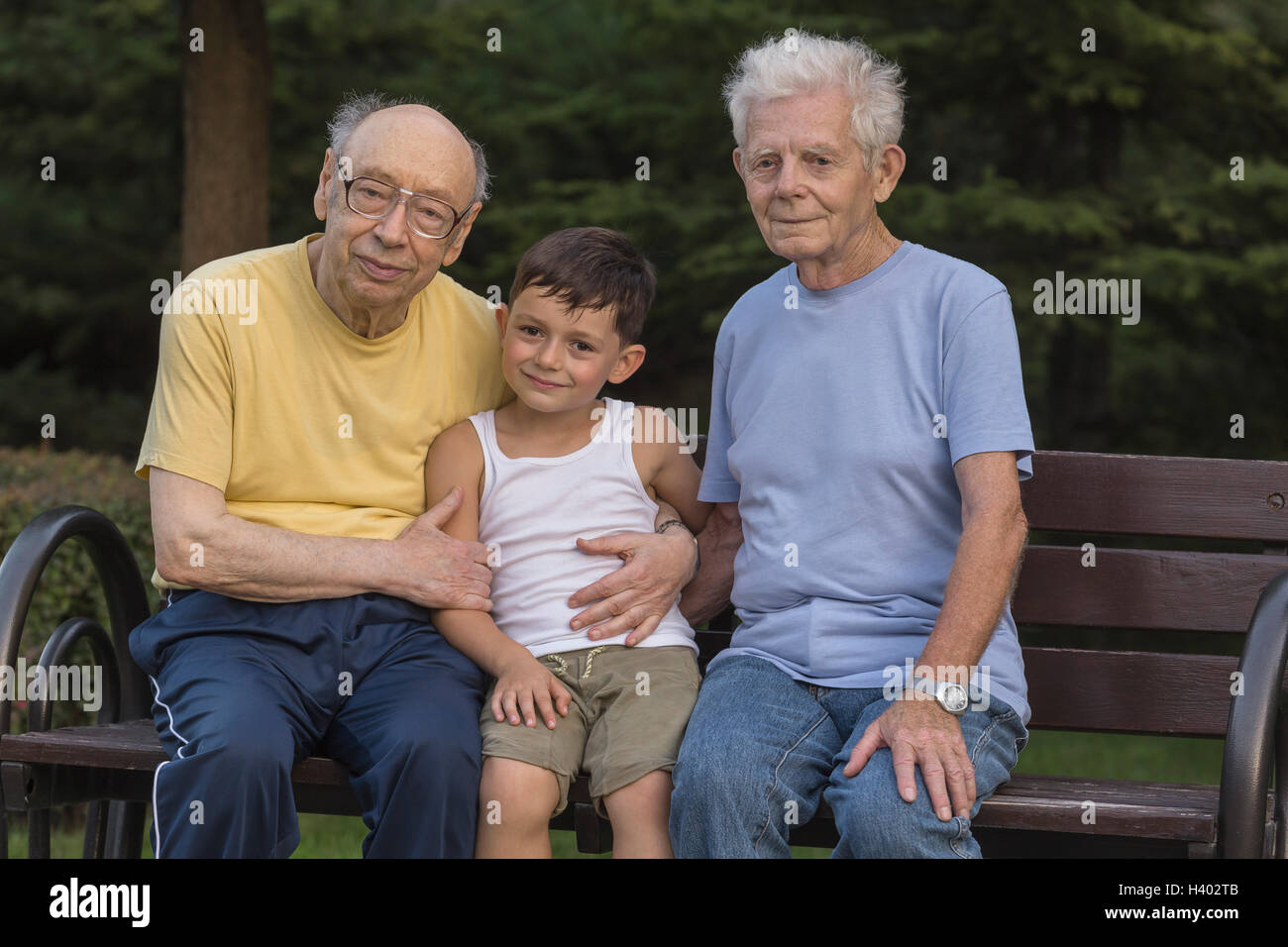 Portrait of smiling boy sitting avec grands-pères au banc de parc Banque D'Images