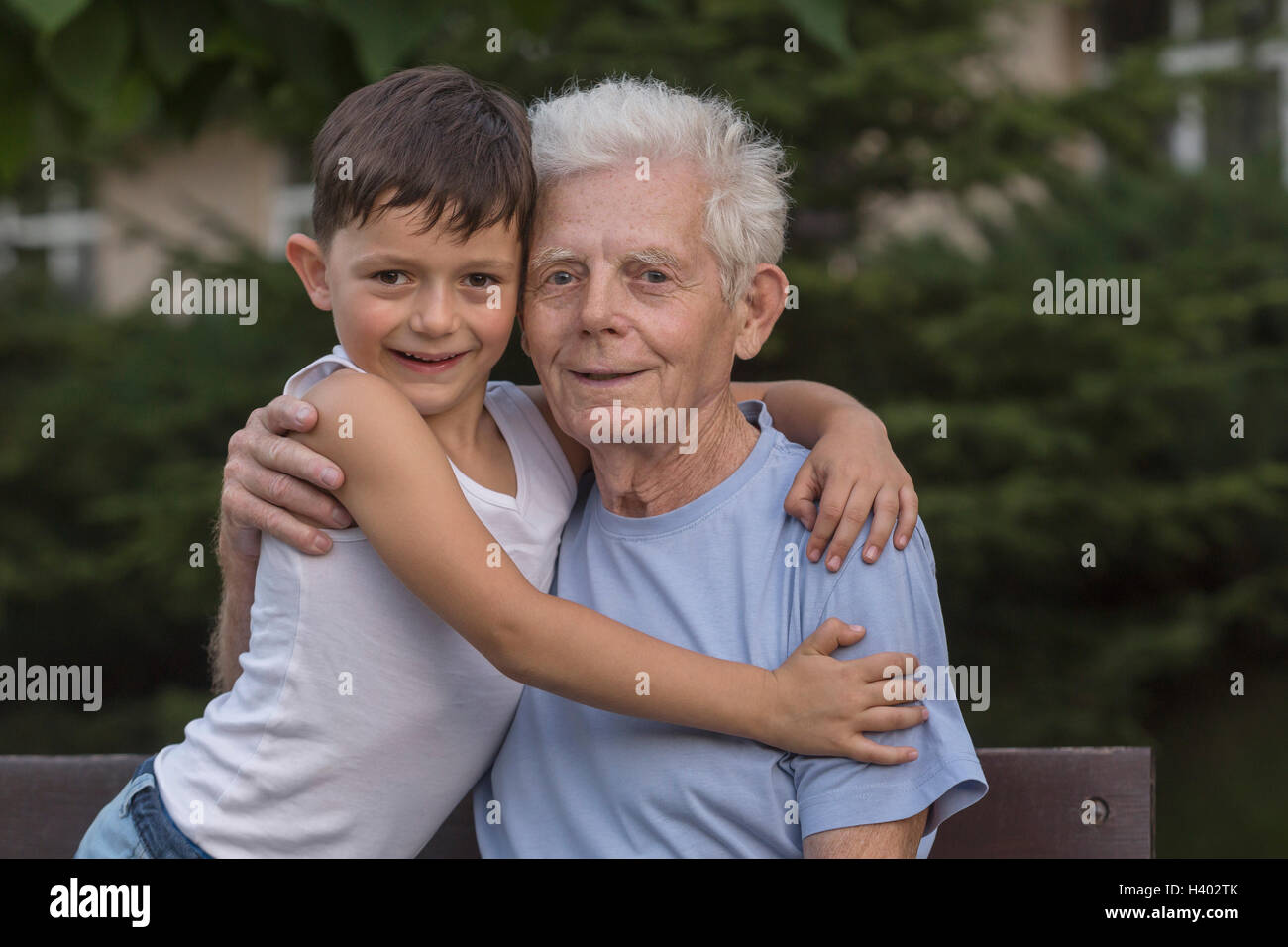 Portrait of smiling grandfather and grandson embrassant assis à banc de parc Banque D'Images