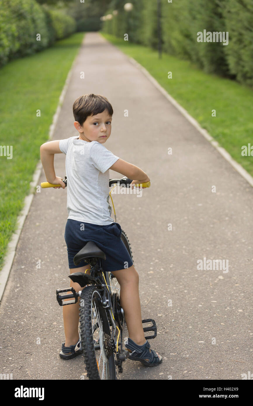 Cute boy le cyclisme sur route au milieu de terrain herbeux dans park Banque D'Images