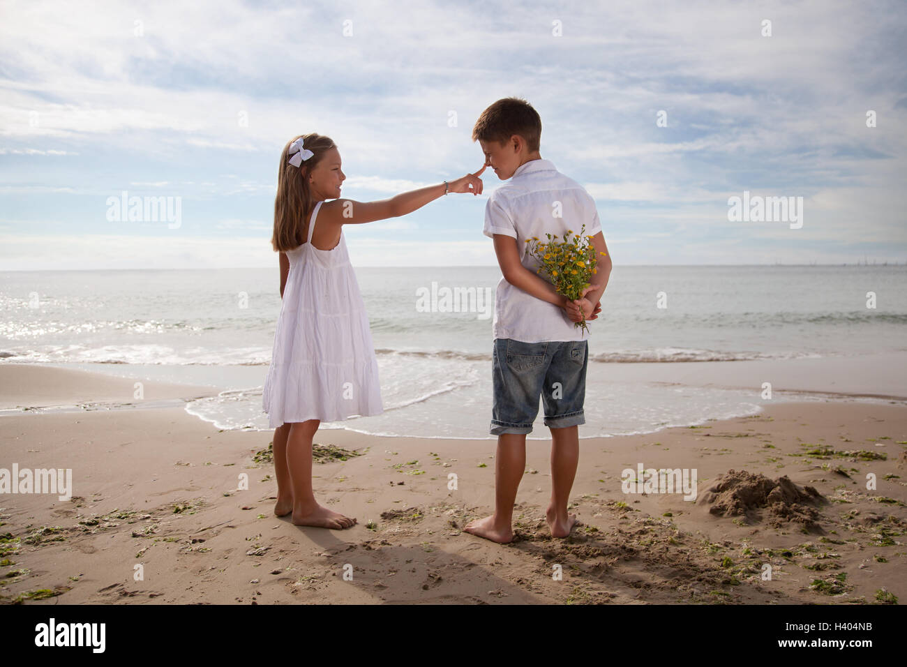 Boy holding Flowers derrière son dos, debout à côté de fille sur la plage Banque D'Images