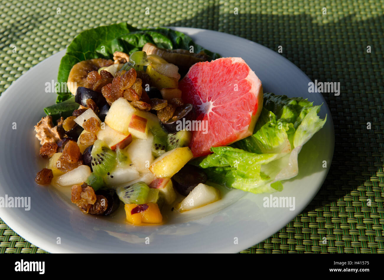 Assiette de dés de fruits mélangés sur lit de légumes verts Banque D'Images