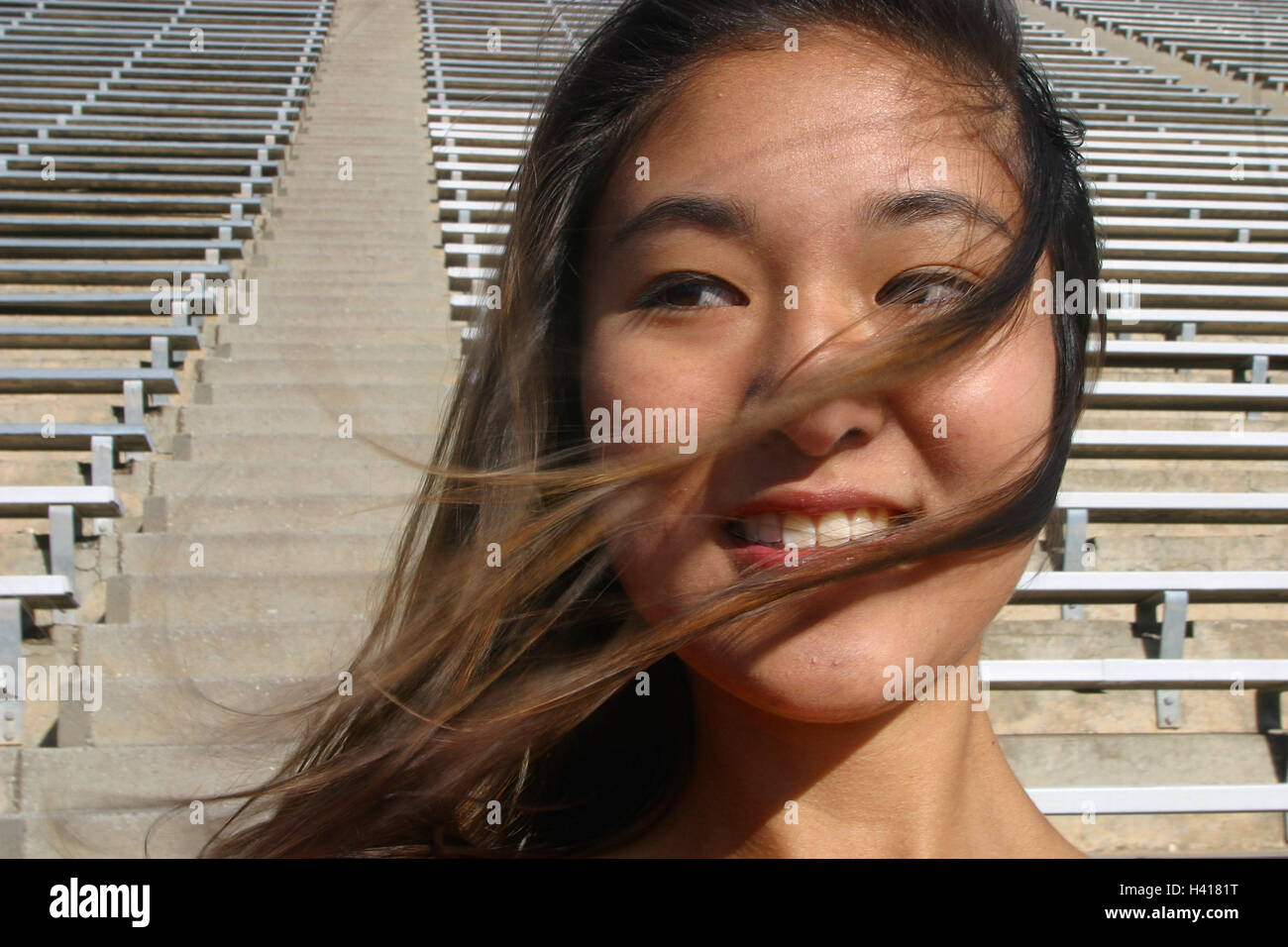 Femme, jeune, sourire, regarder, cheveux brins, l'arrière-plan, stand, portrait, portrait de femmes, jeunes, Asiatique, Asiatique, vue latérale, vent, venteux, poils, blow, poil long, brun, gaieté, la satisfaction, les lignes, les sports stadium, stade, seat possi Banque D'Images